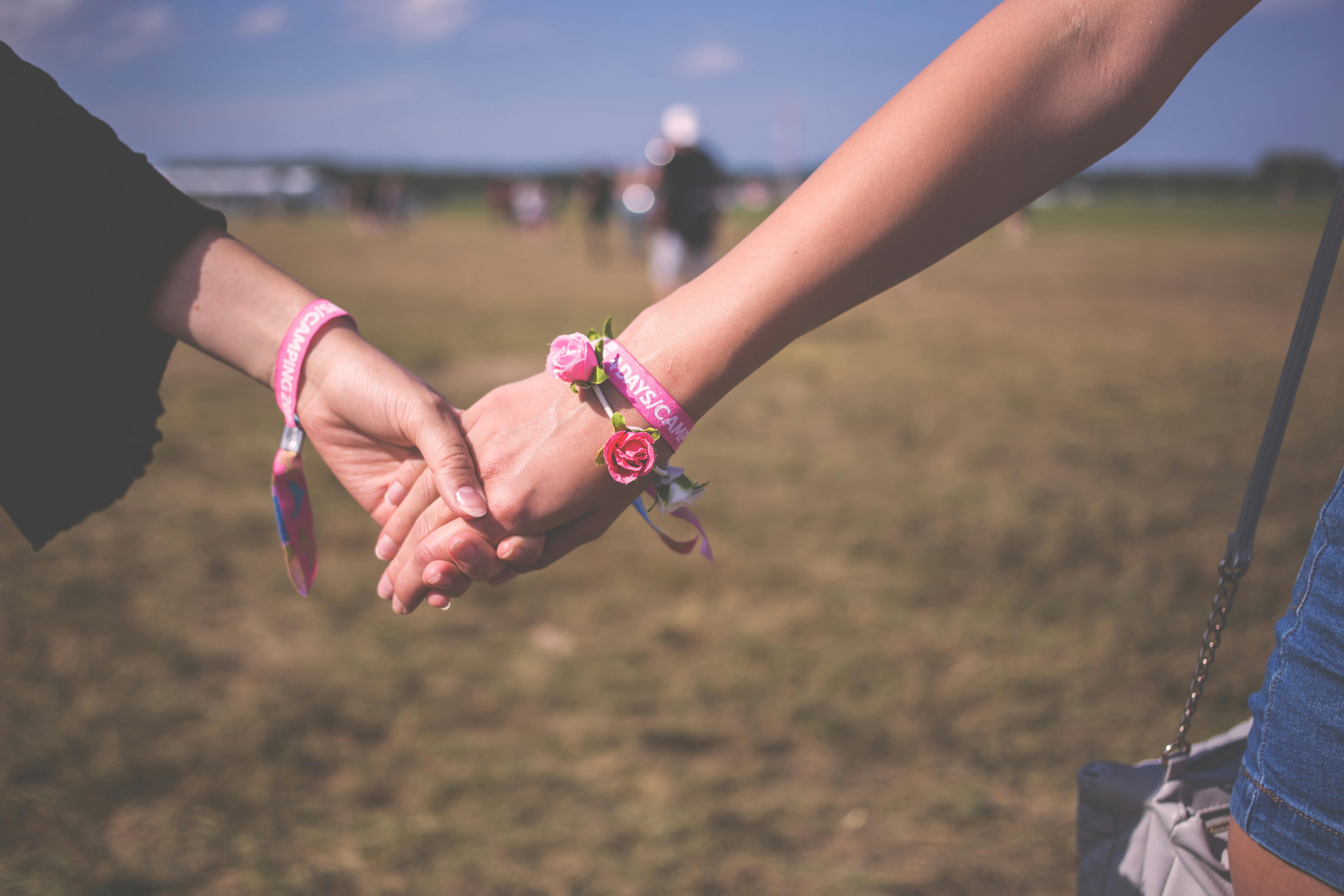 2 person holding each other wearing pink friendship bracelet during daytime