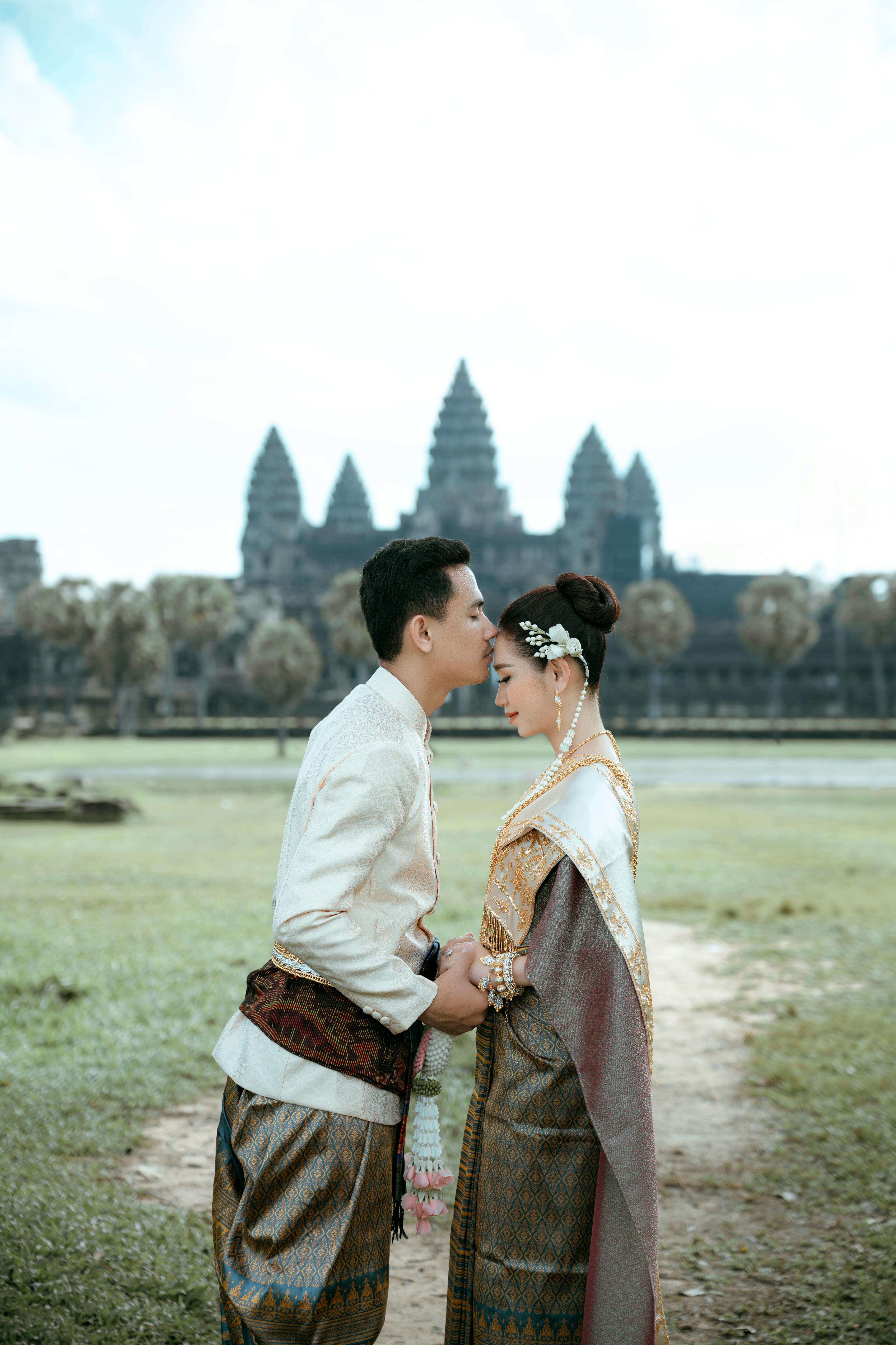 a couple in traditional clothing standing in front of a temple