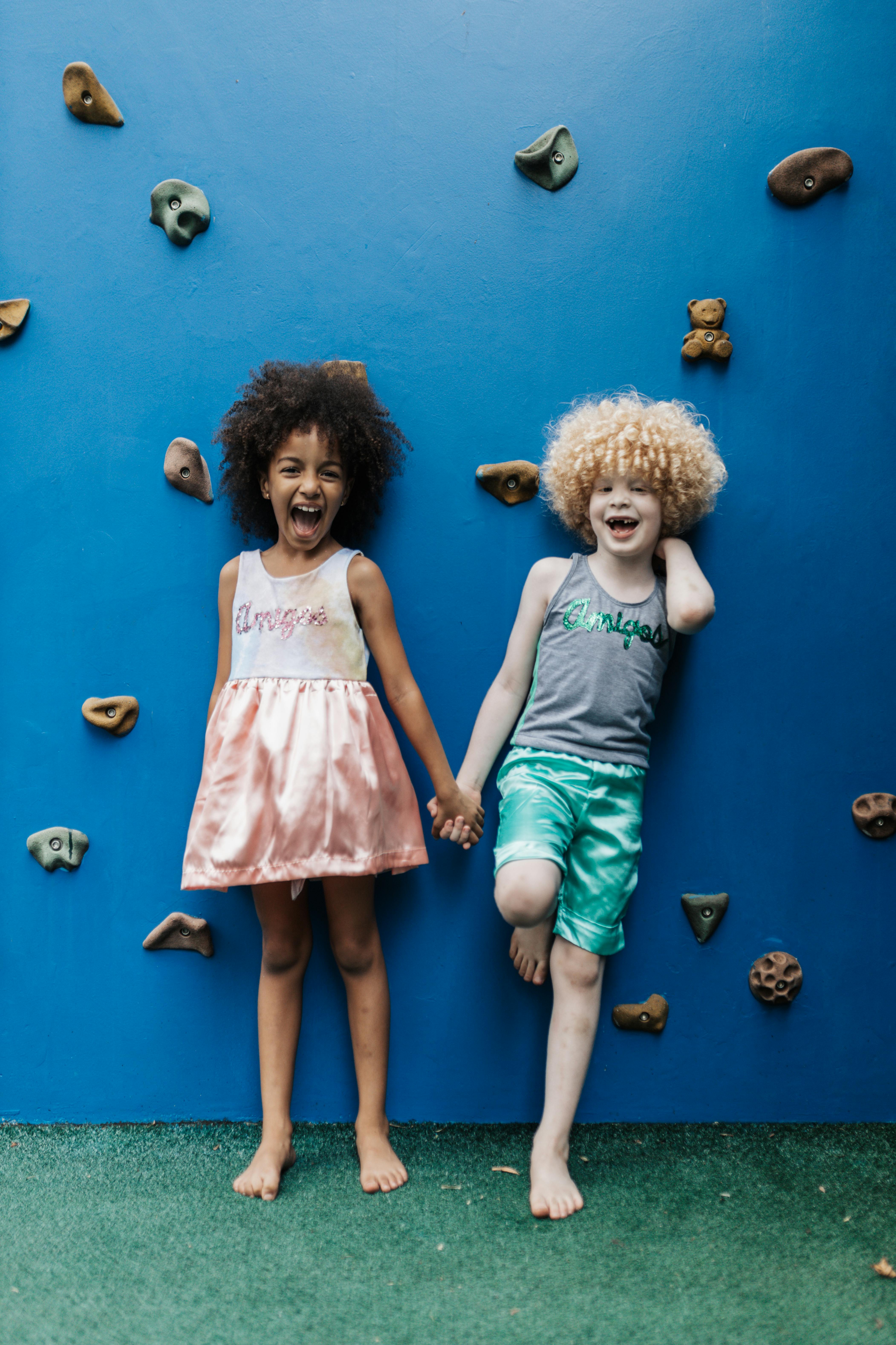 a little girl and boy standing by a rock climbing wall