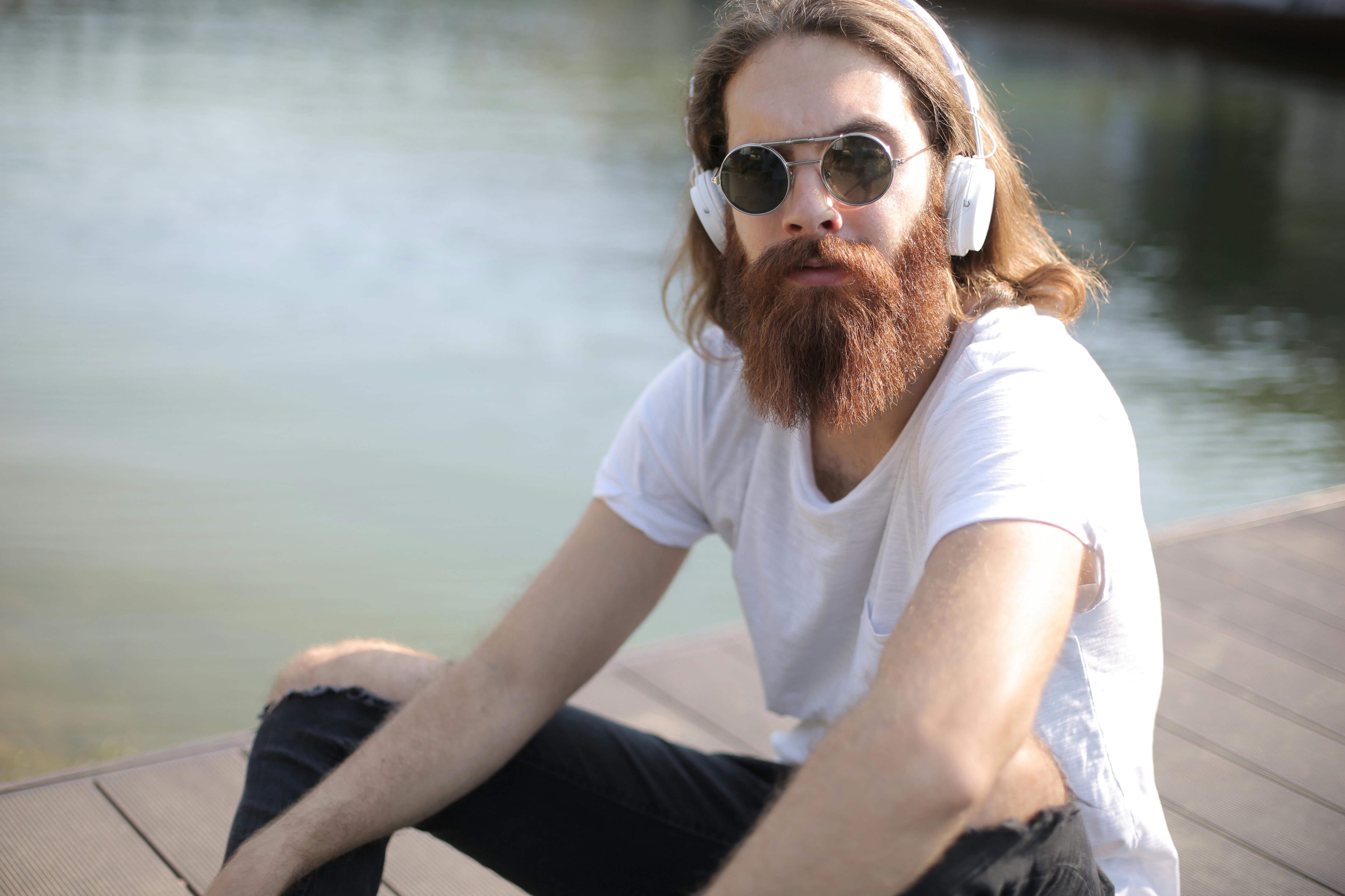 man in white crew neck t shirt wearing brown sunglasses sitting on rock