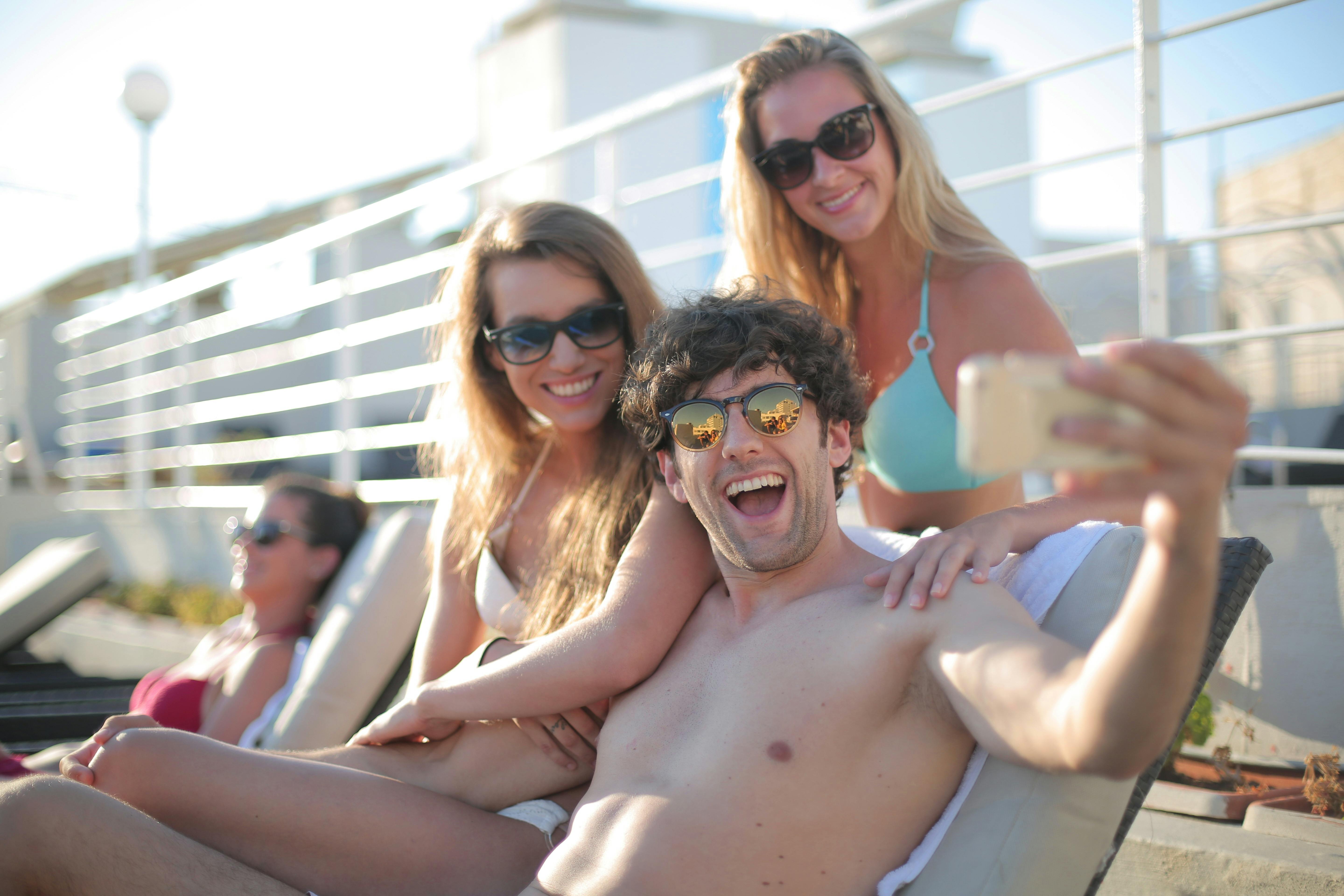 joyful friends taking video on phone while resting on beach