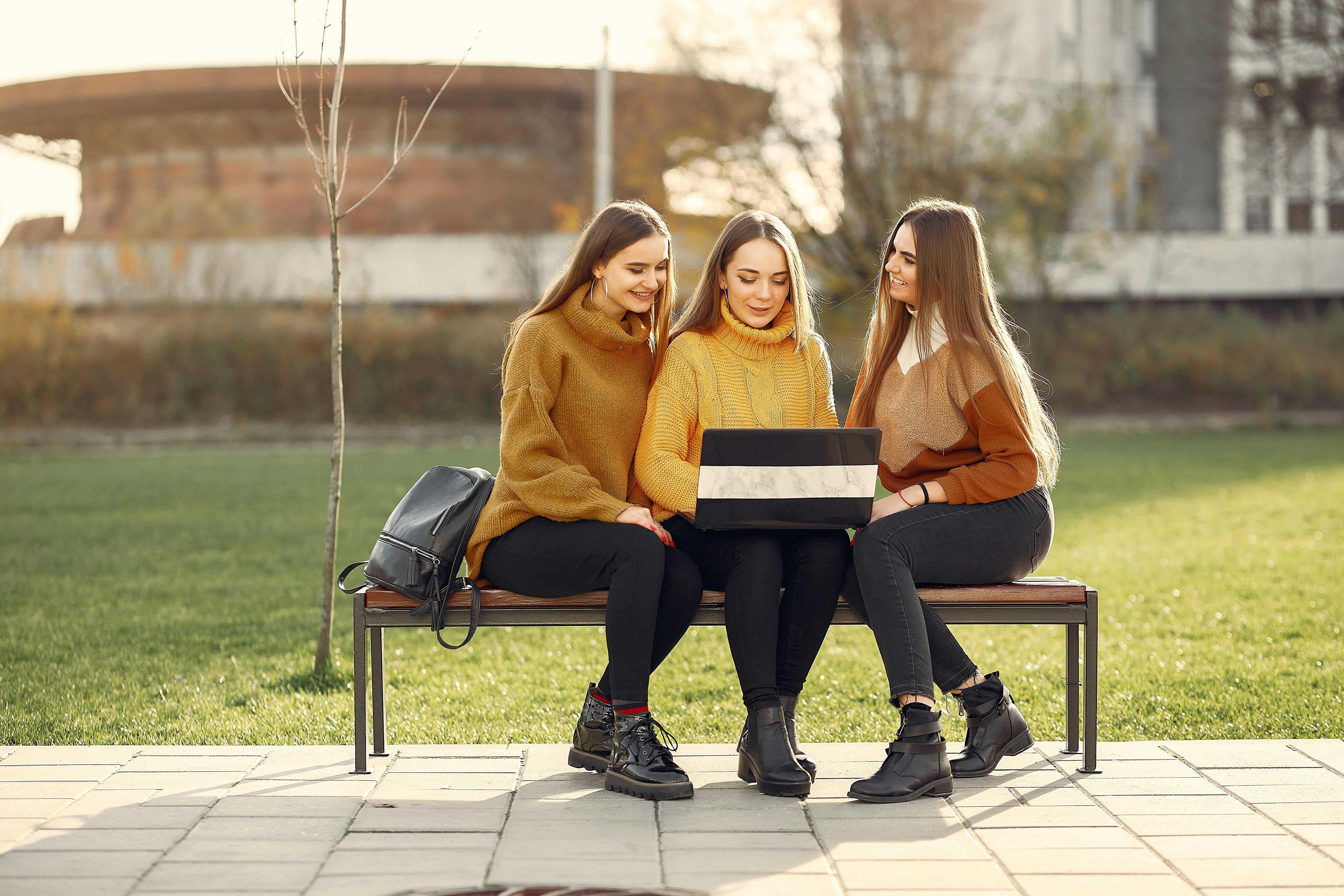 positive girlfriends using laptop on bench