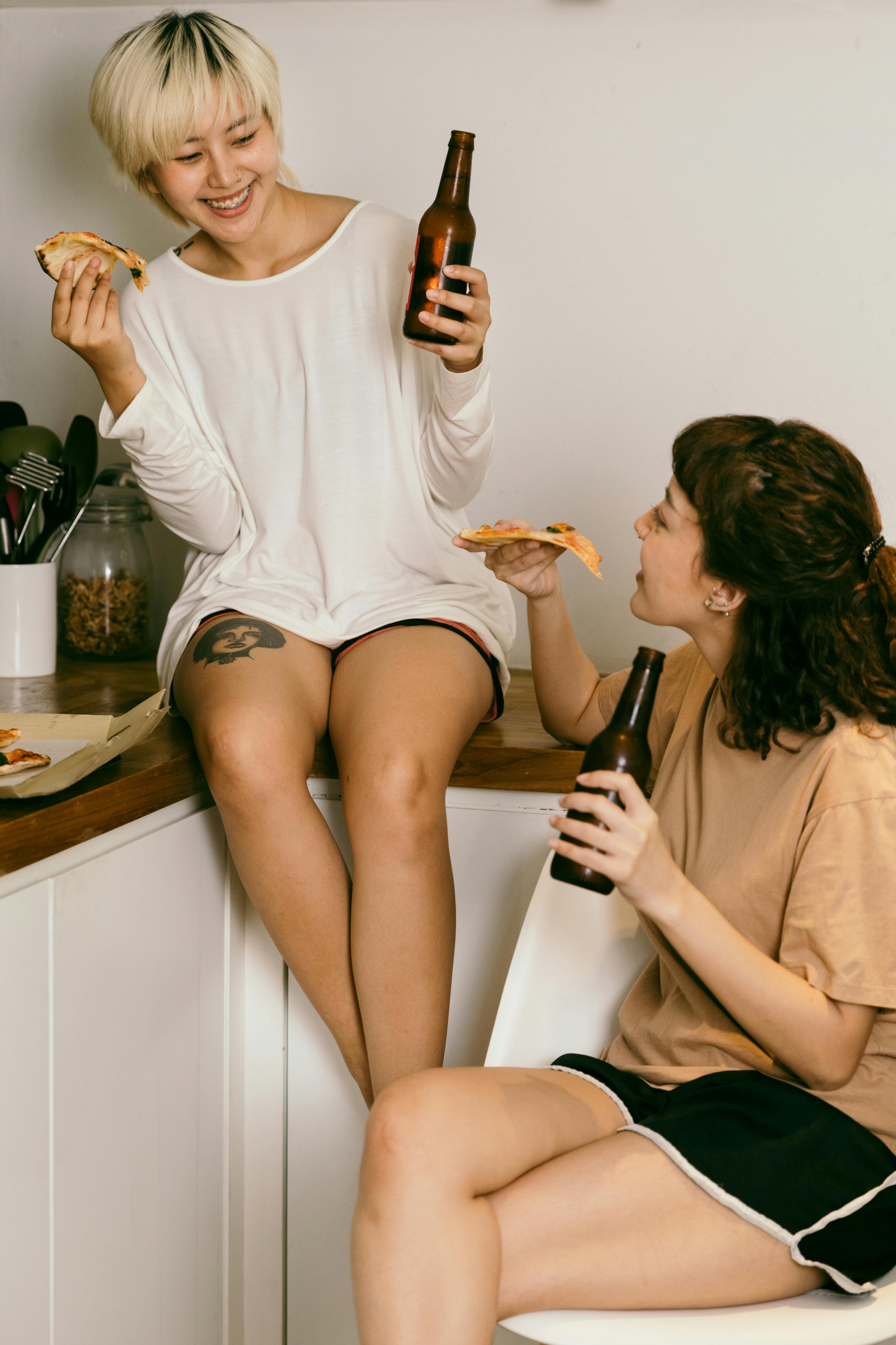 women drinking beer and eating pizza in the kitchen