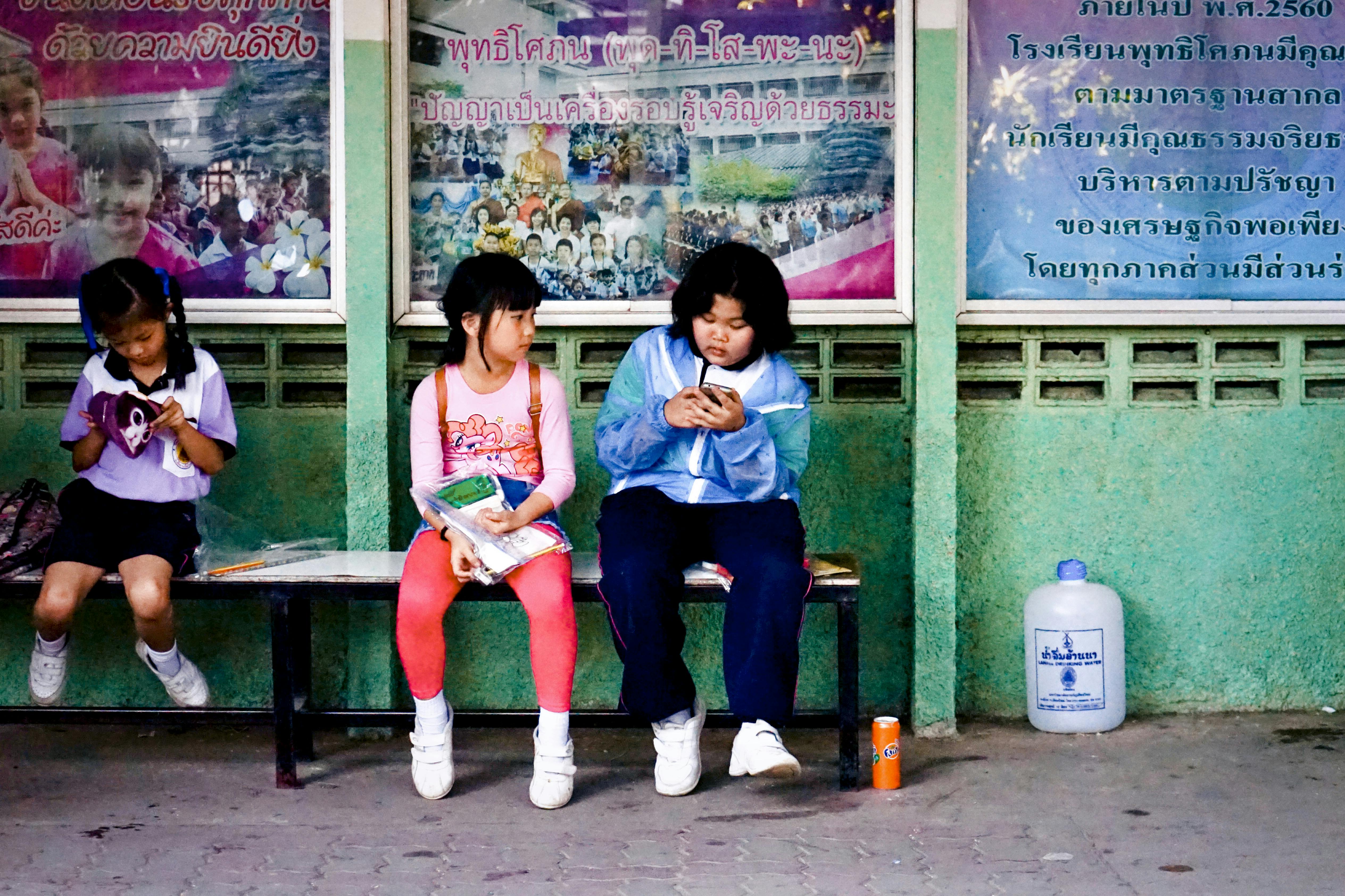 asian schoolkids sitting on bench on street