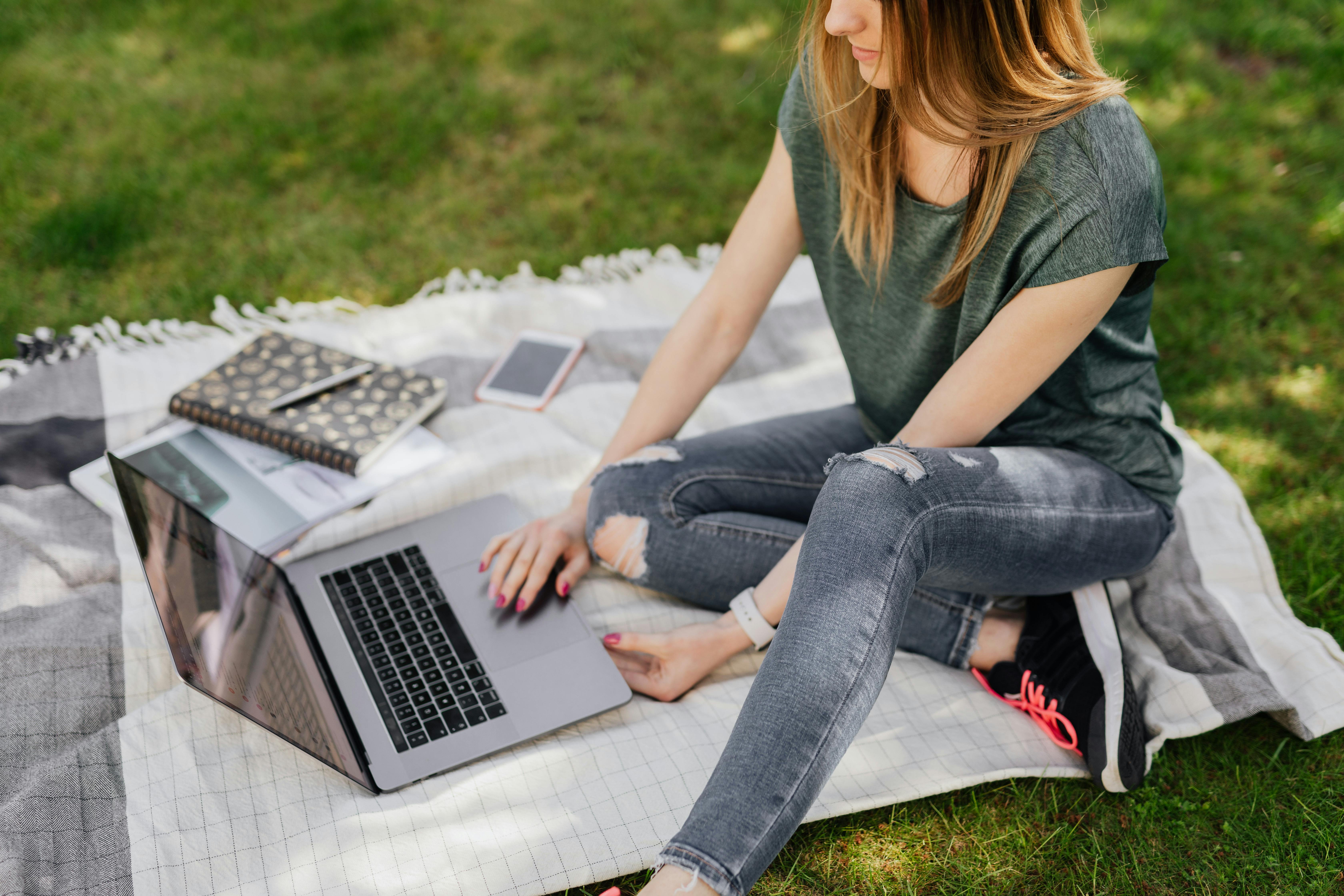 student doing home assignments on laptop while sitting in park