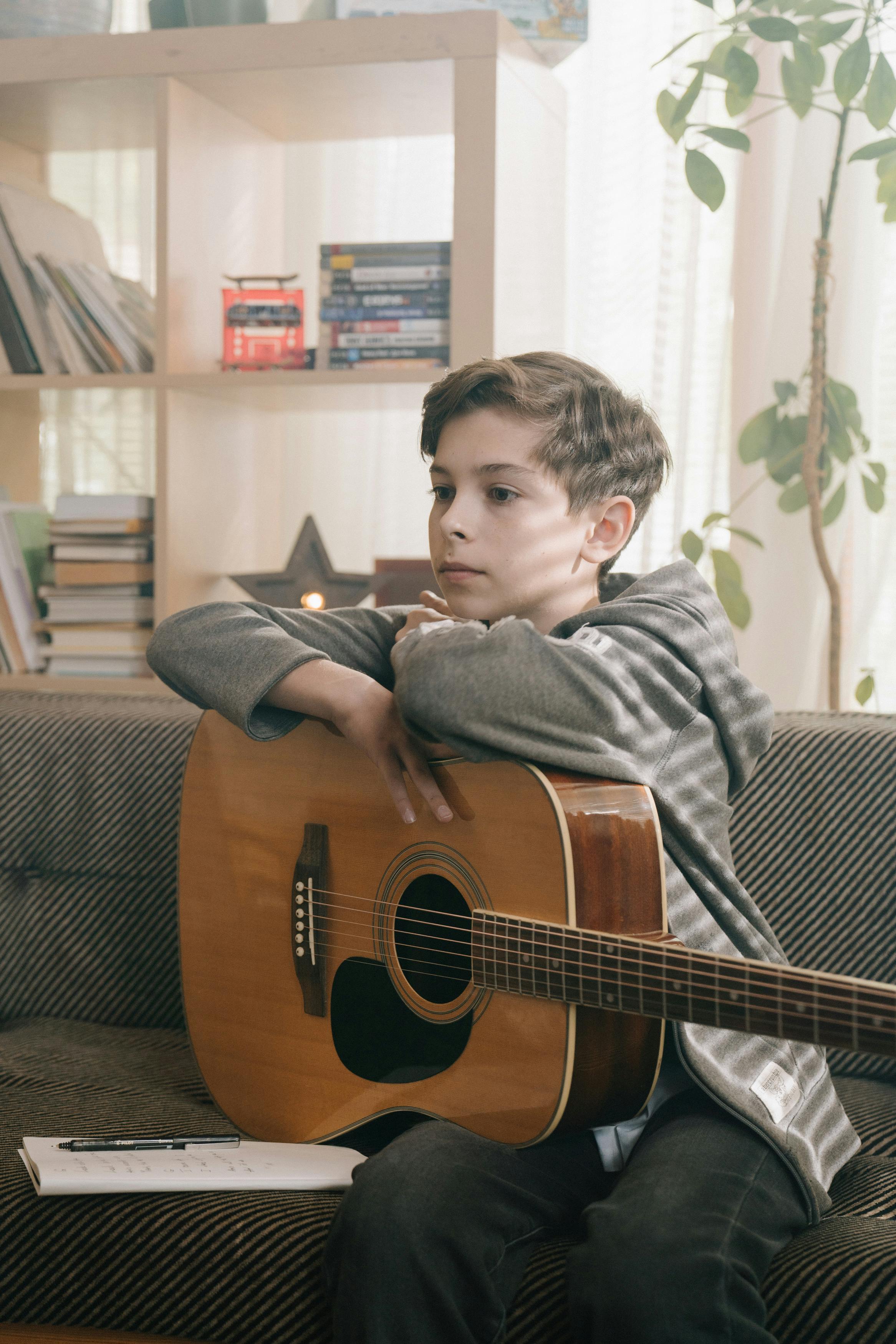 boy in gray and black stripe long sleeve shirt playing brown acoustic guitar