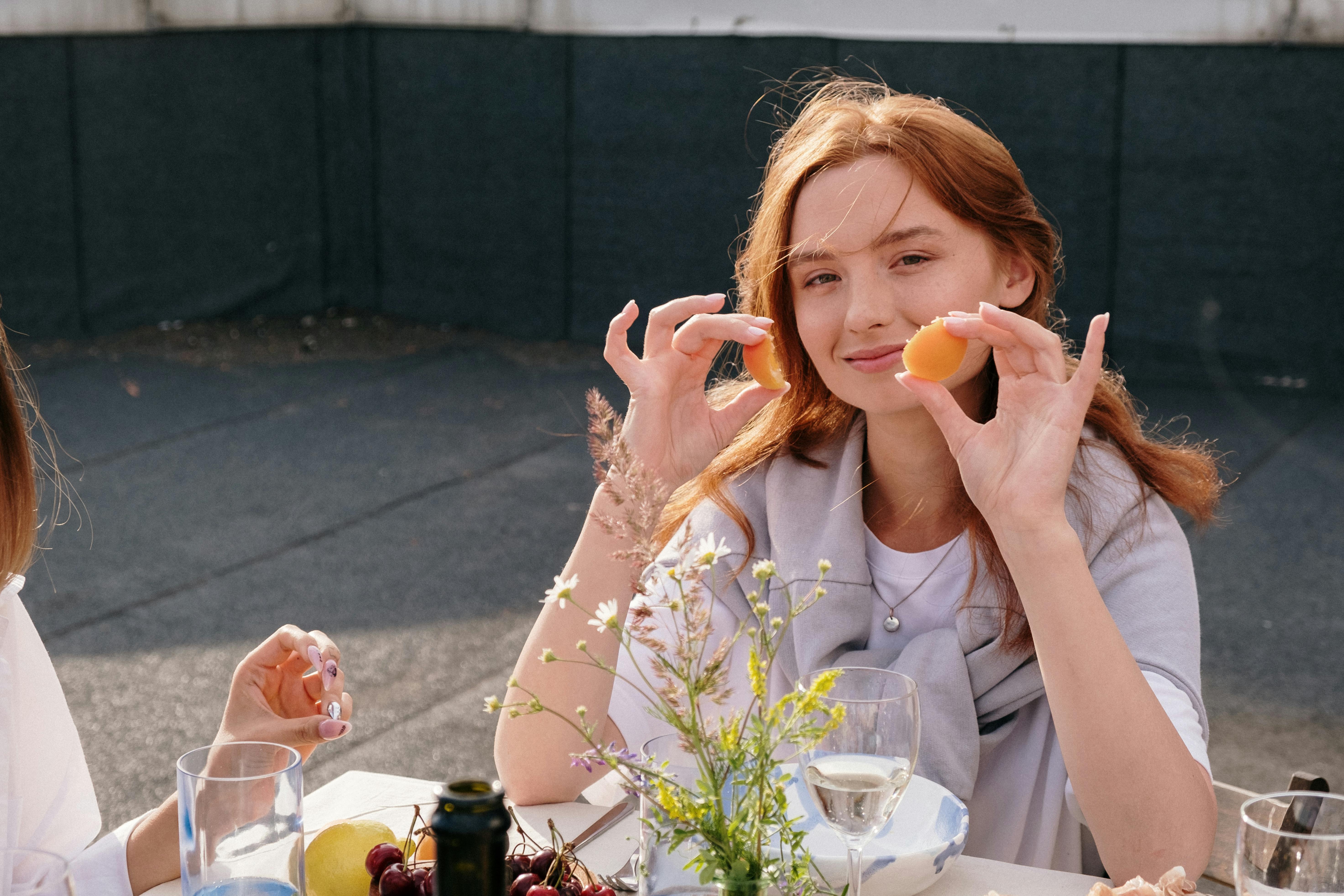 woman in white dress shirt holding orange fruit