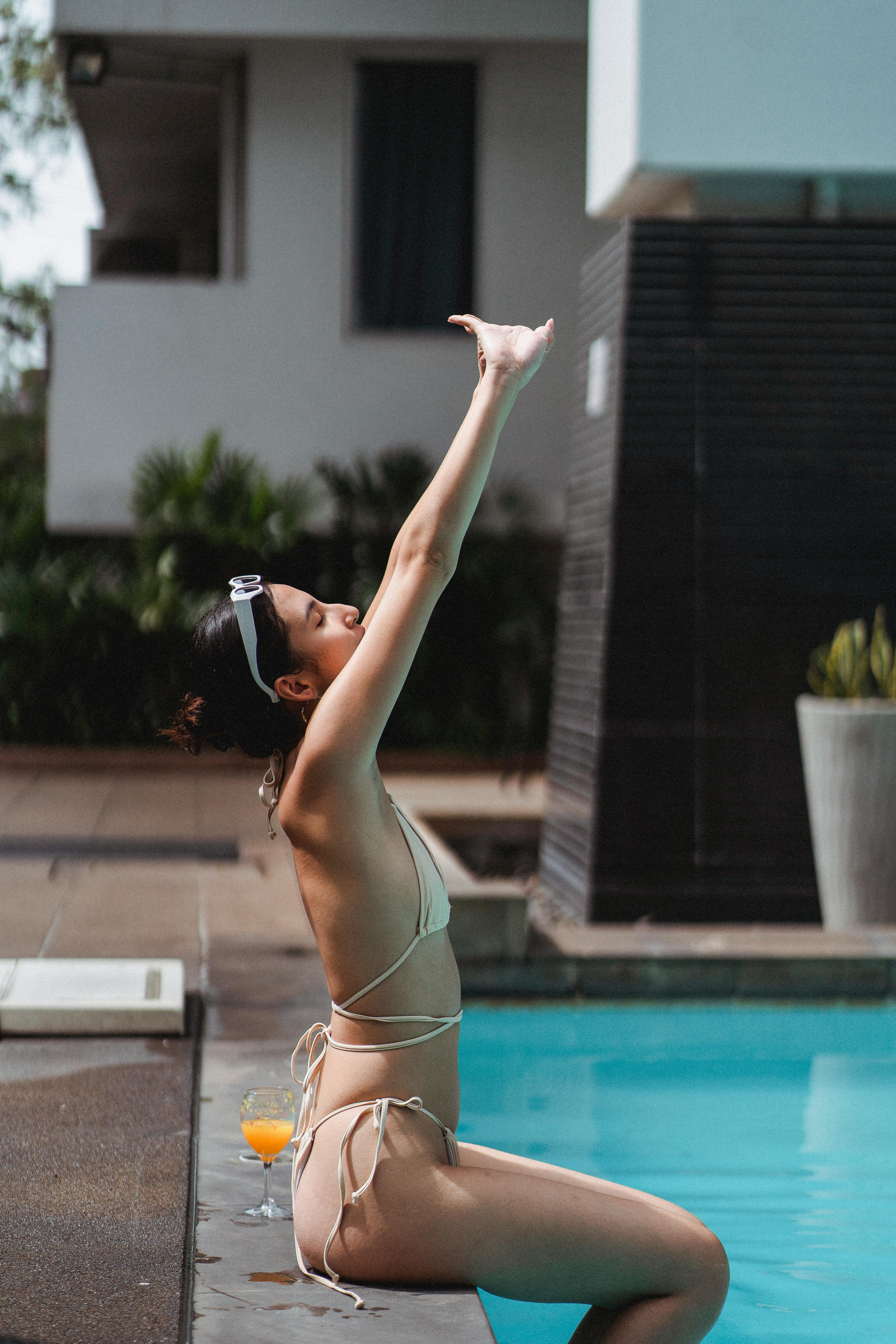 relaxed young ethnic woman raising arms while sunbathing at poolside