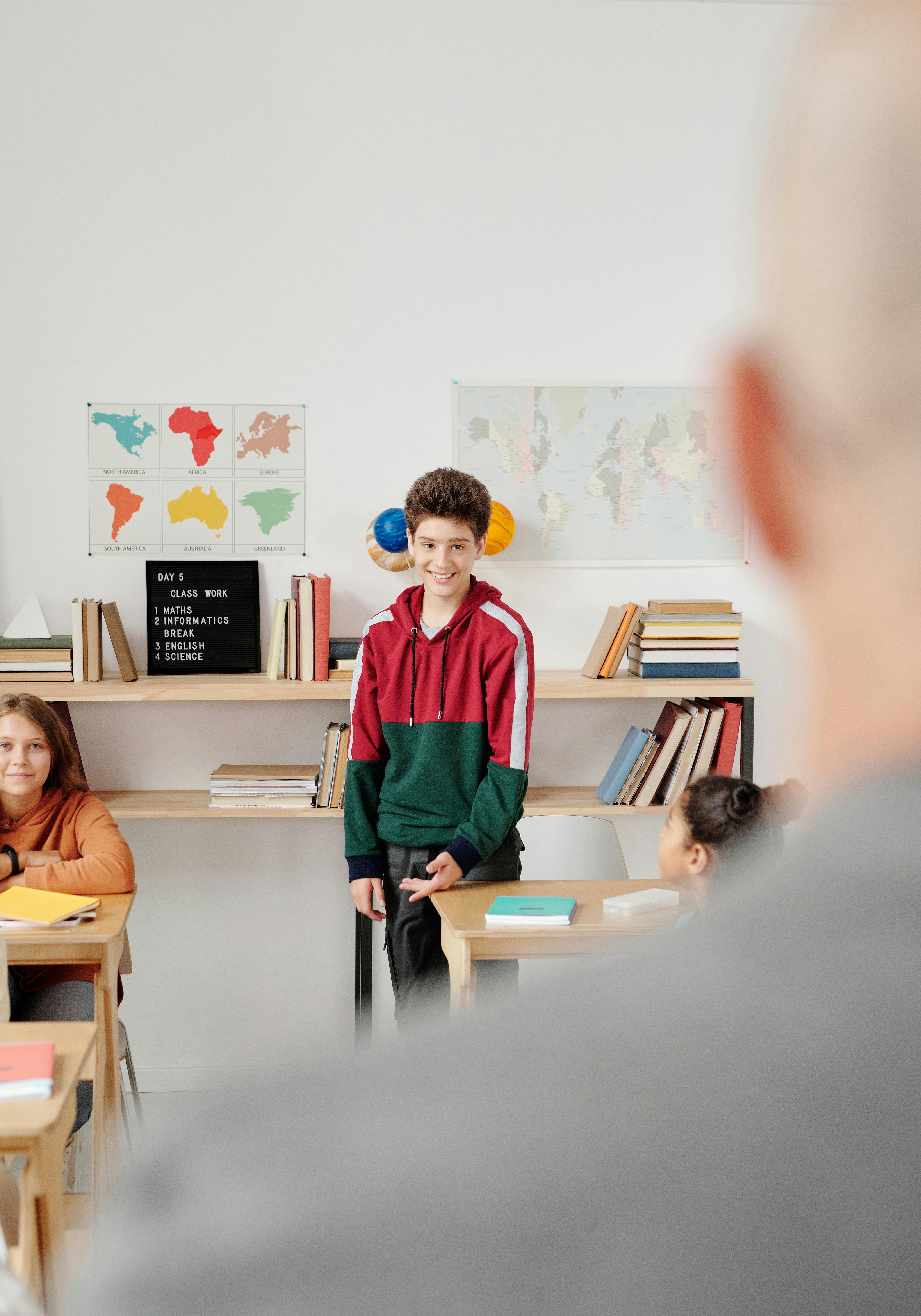 boy in red and green hoodie standing in the classroom