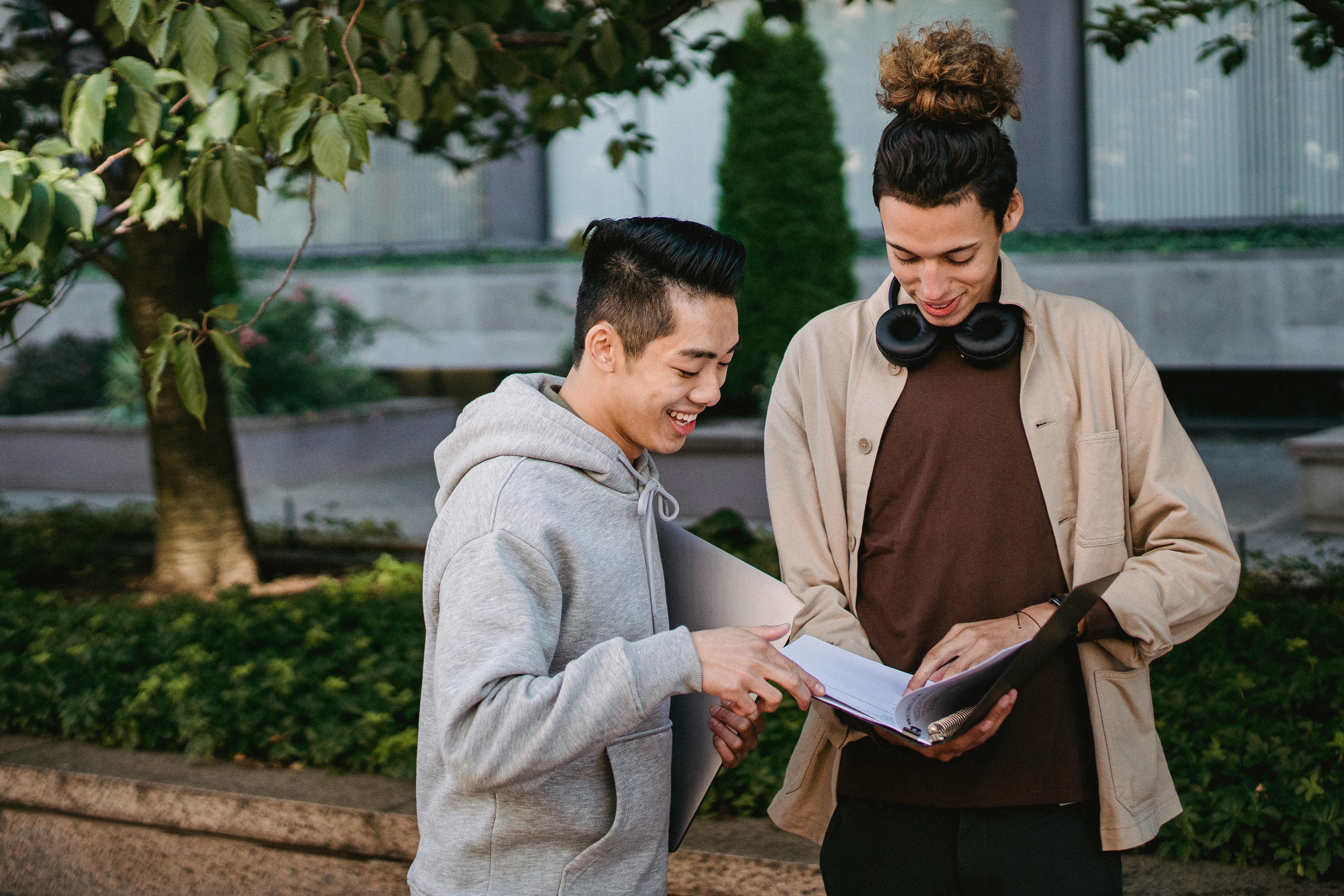 cheerful multiethnic male students reading textbook in park