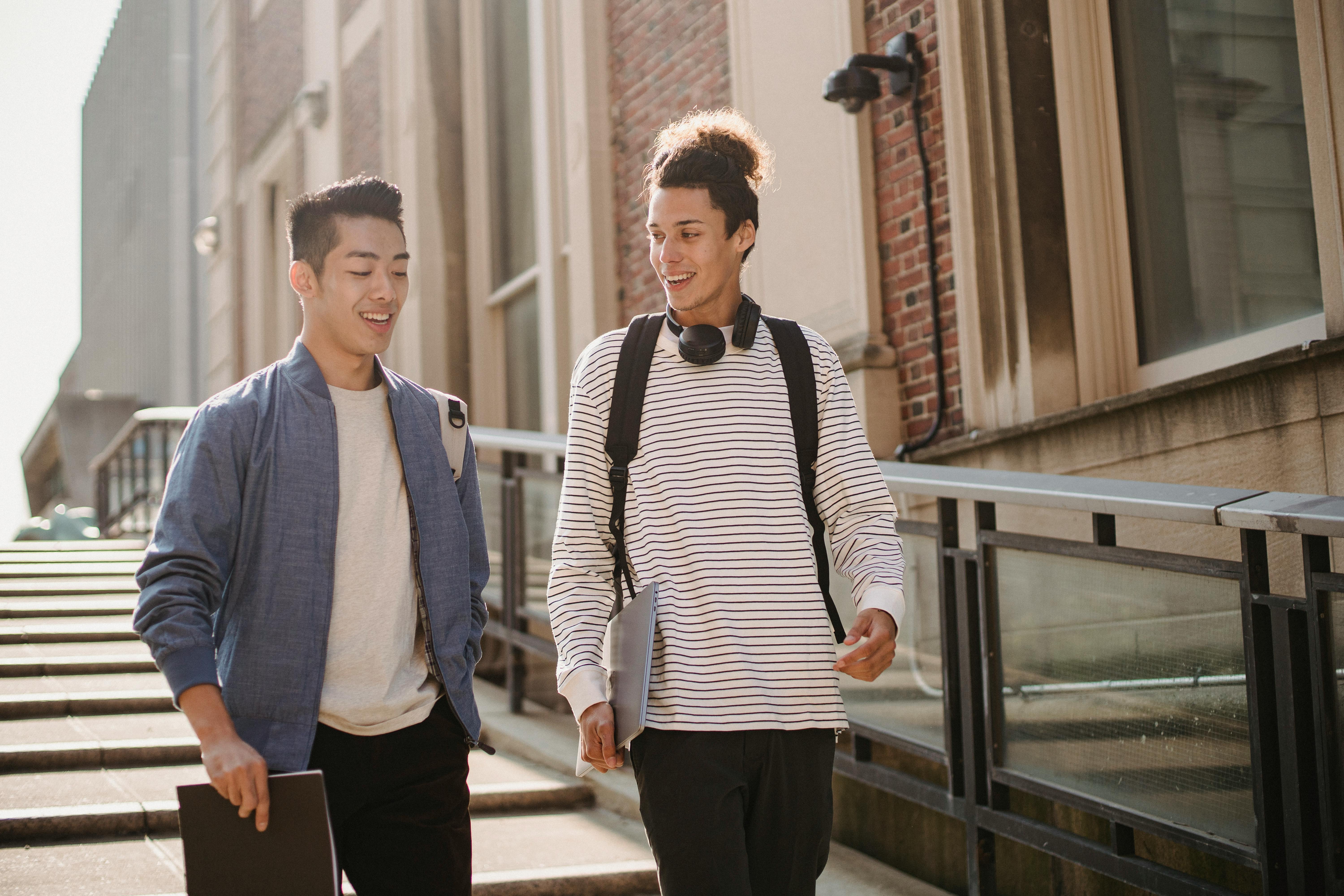 cheerful multiethnic students walking downstairs with gadget