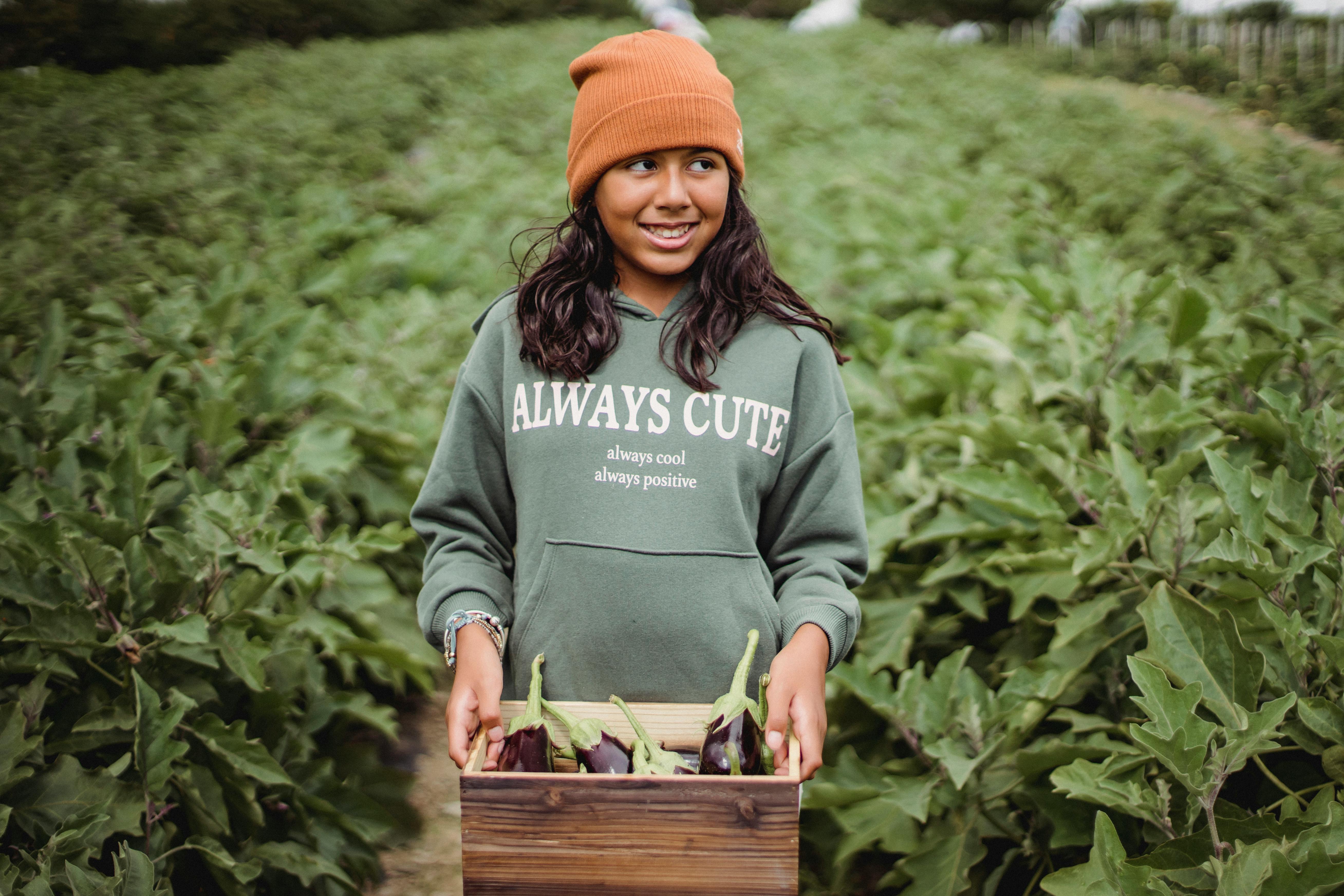 cheerful ethnic girl with eggplants in box on farm