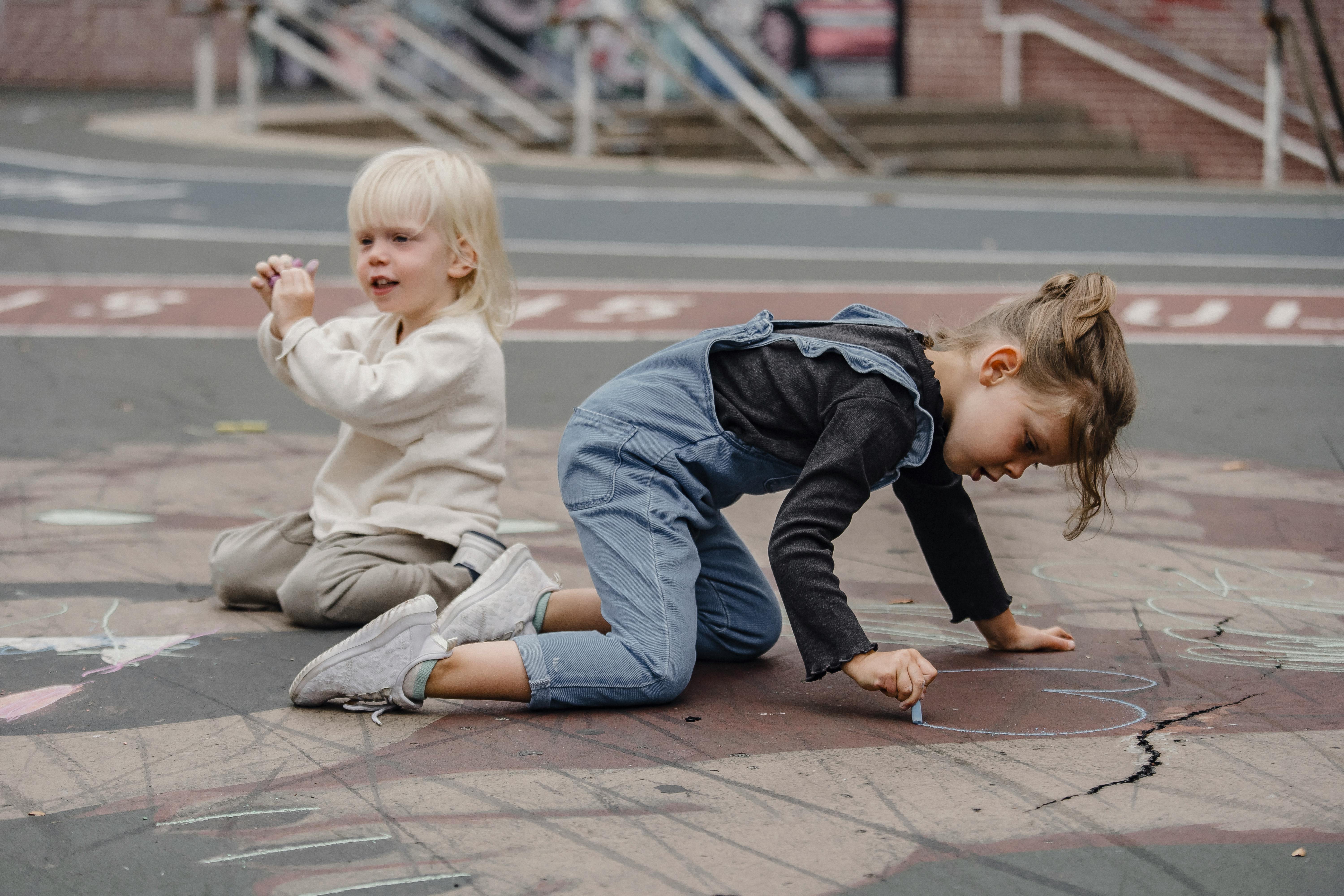 concentrated kids with chalks on asphalt