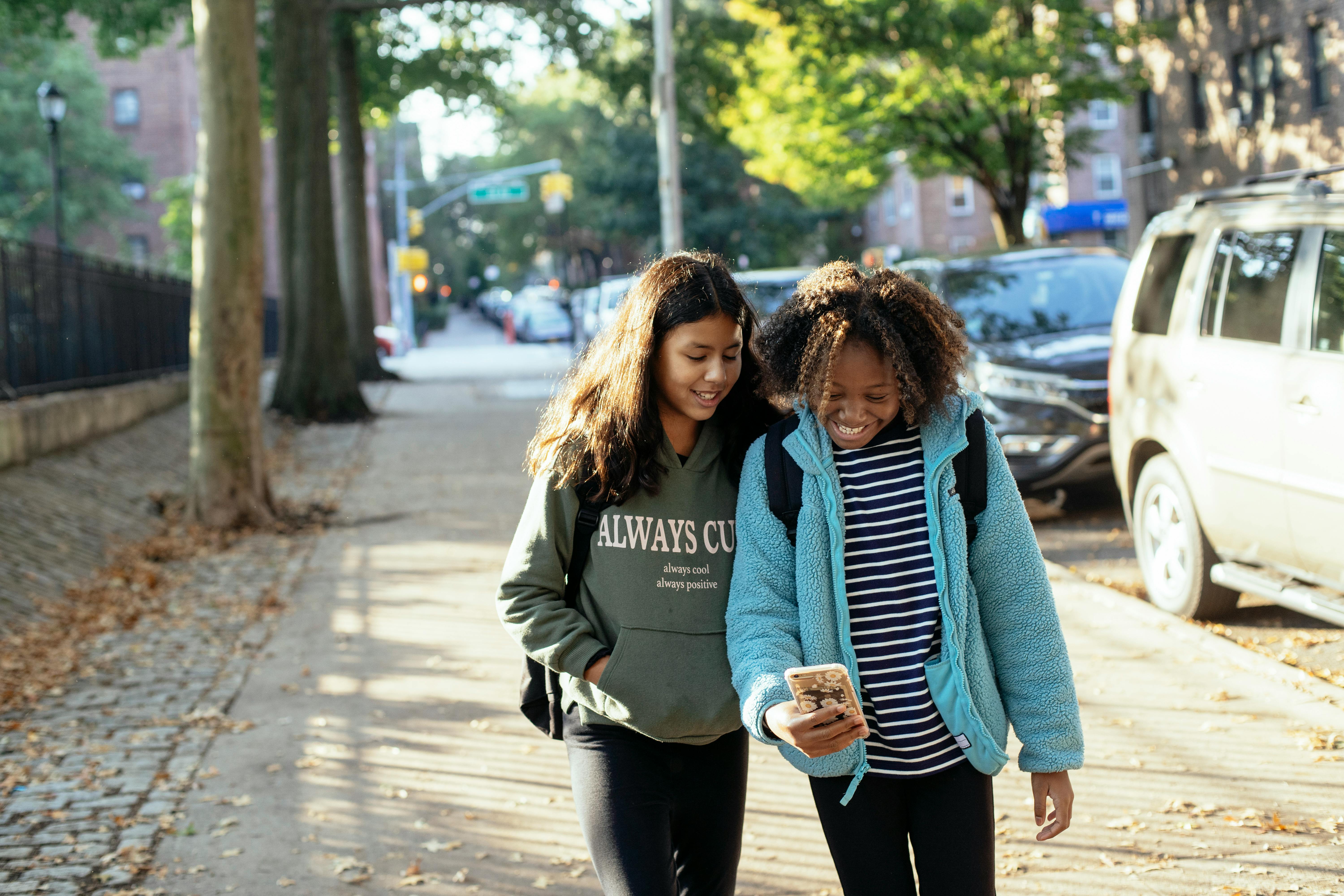 happy multiethnic girlfriends with smartphone on street