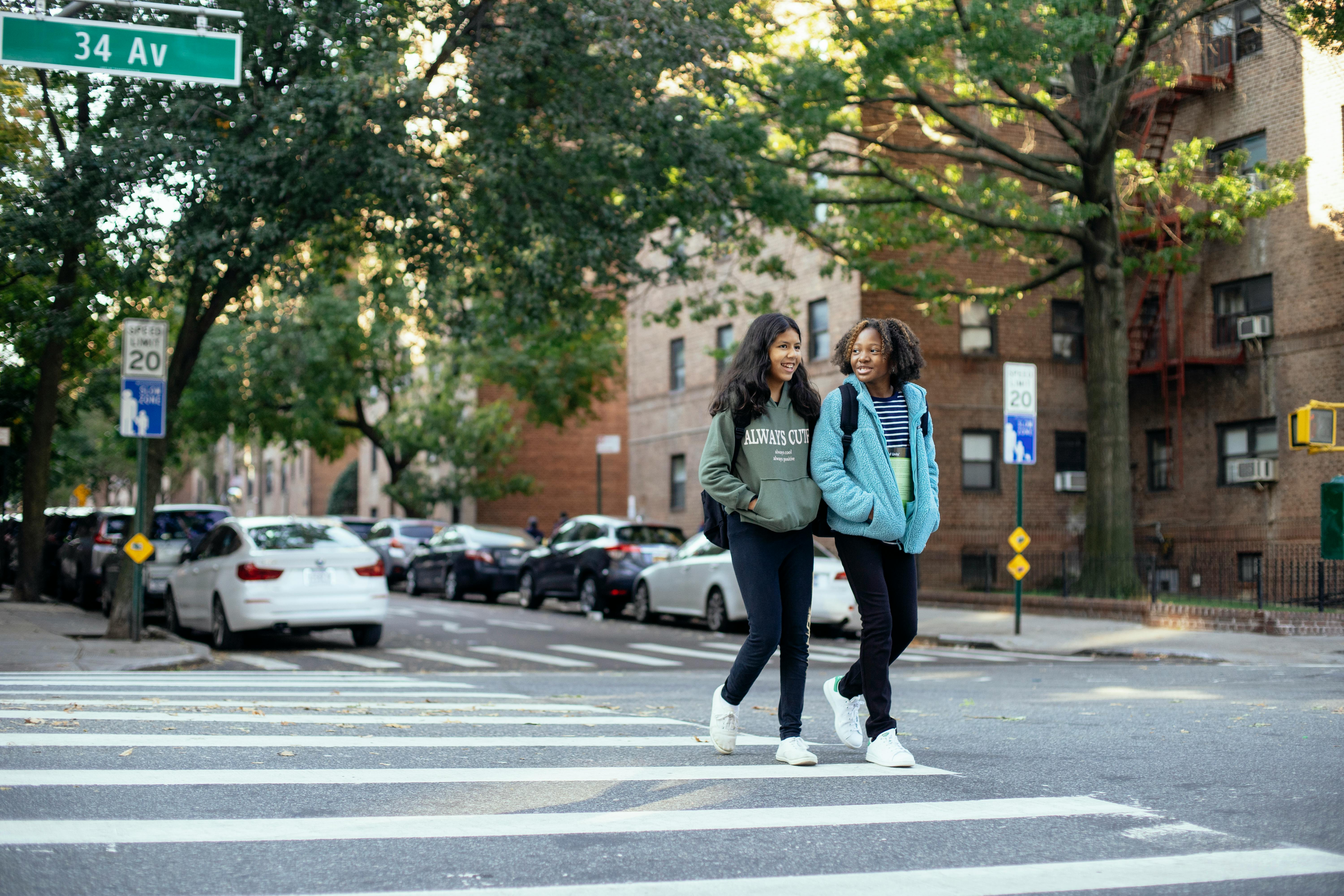 cheerful schoolgirls crossing road in city