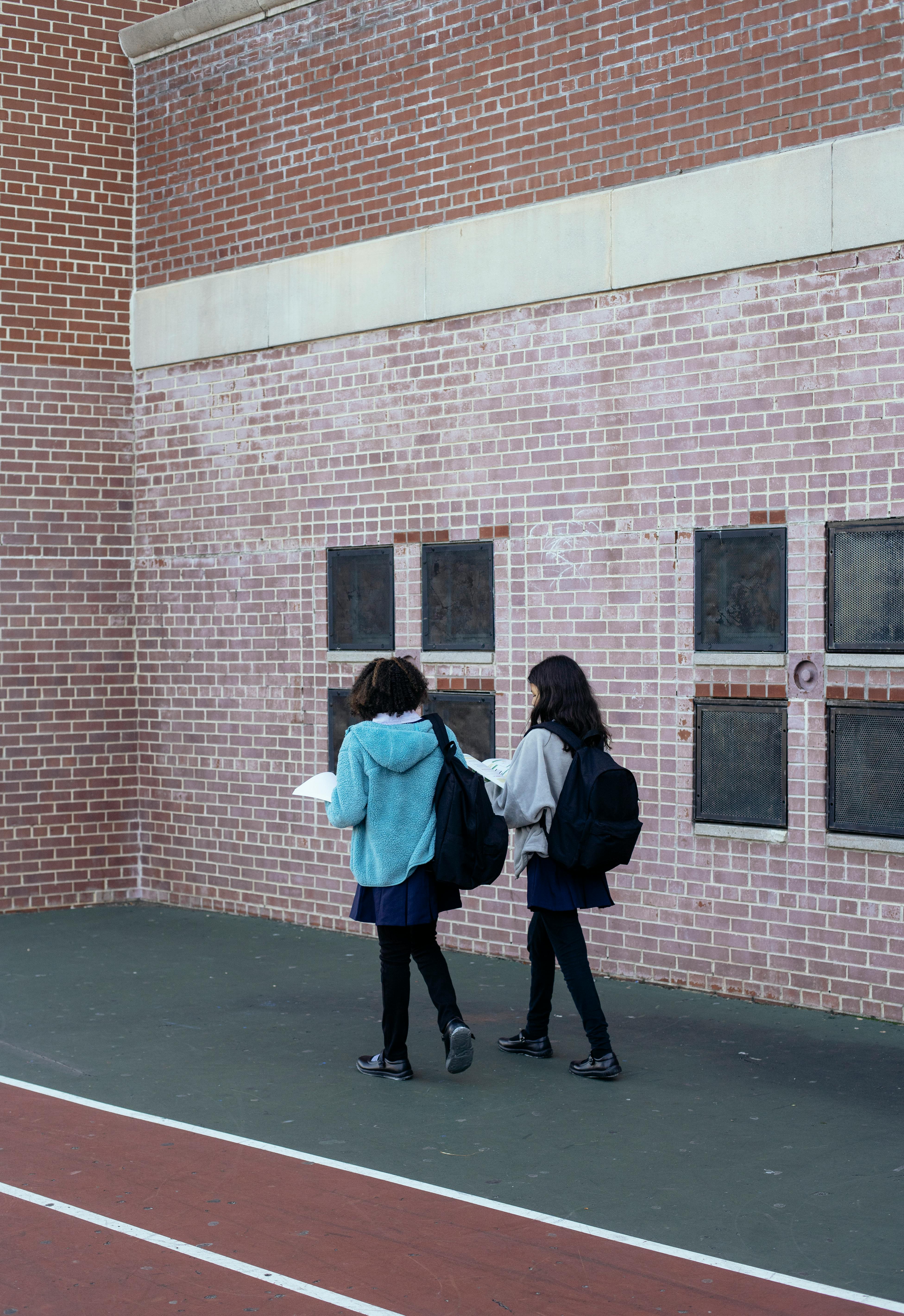 girls with backpacks discussing homework near school