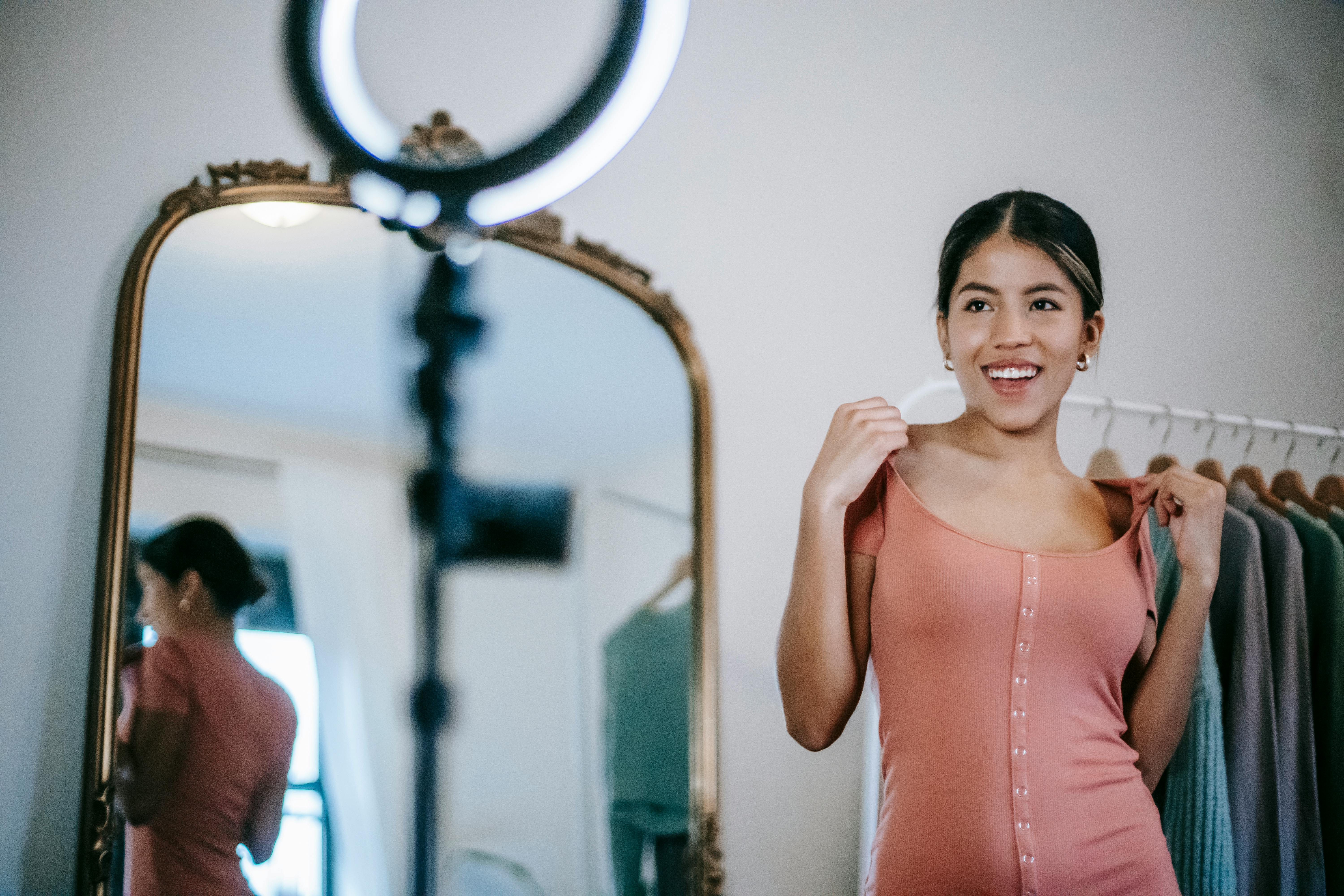 happy ethnic lady filming video on phone while demonstrating dress