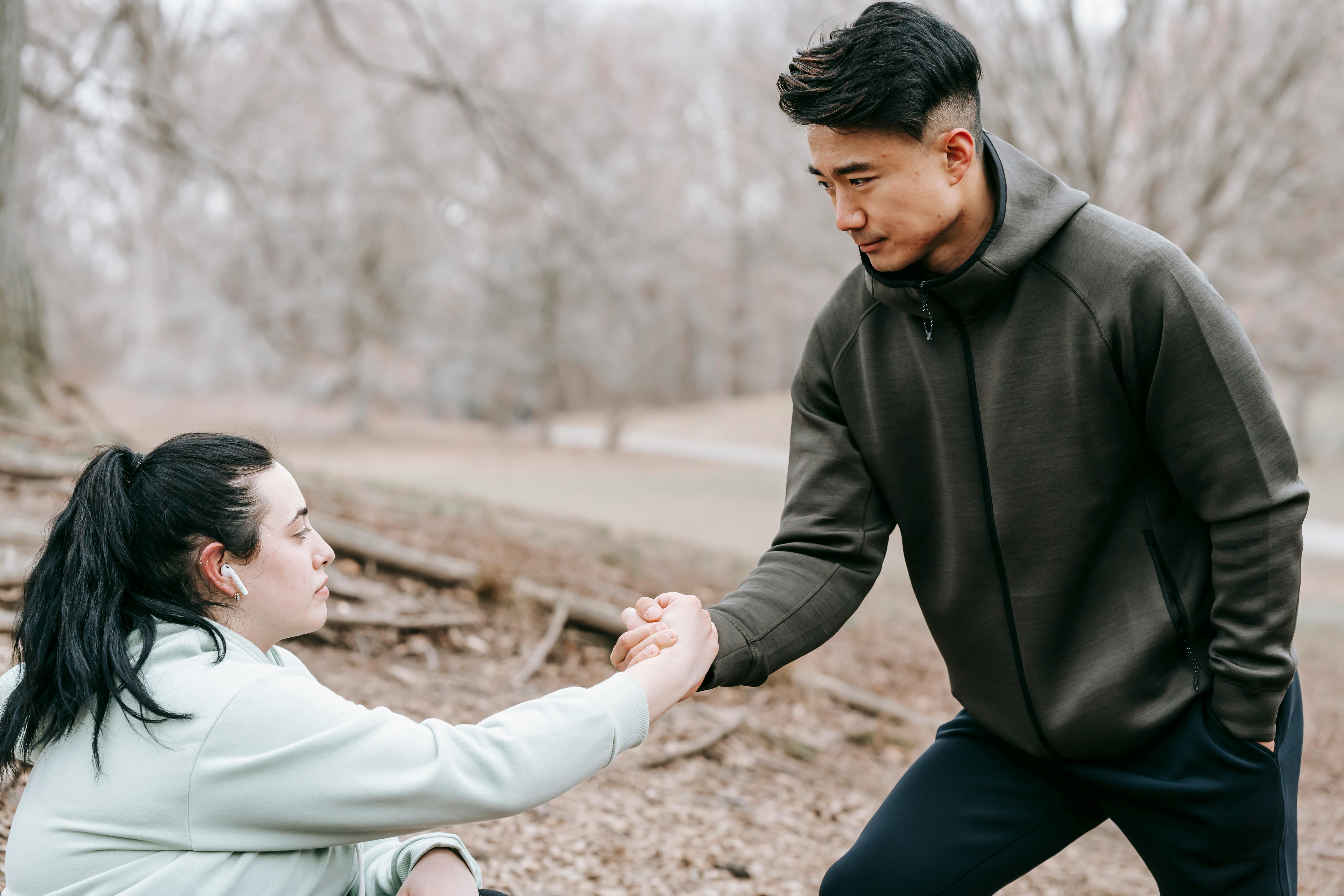 asian sportsman helping fell woman to get up from ground