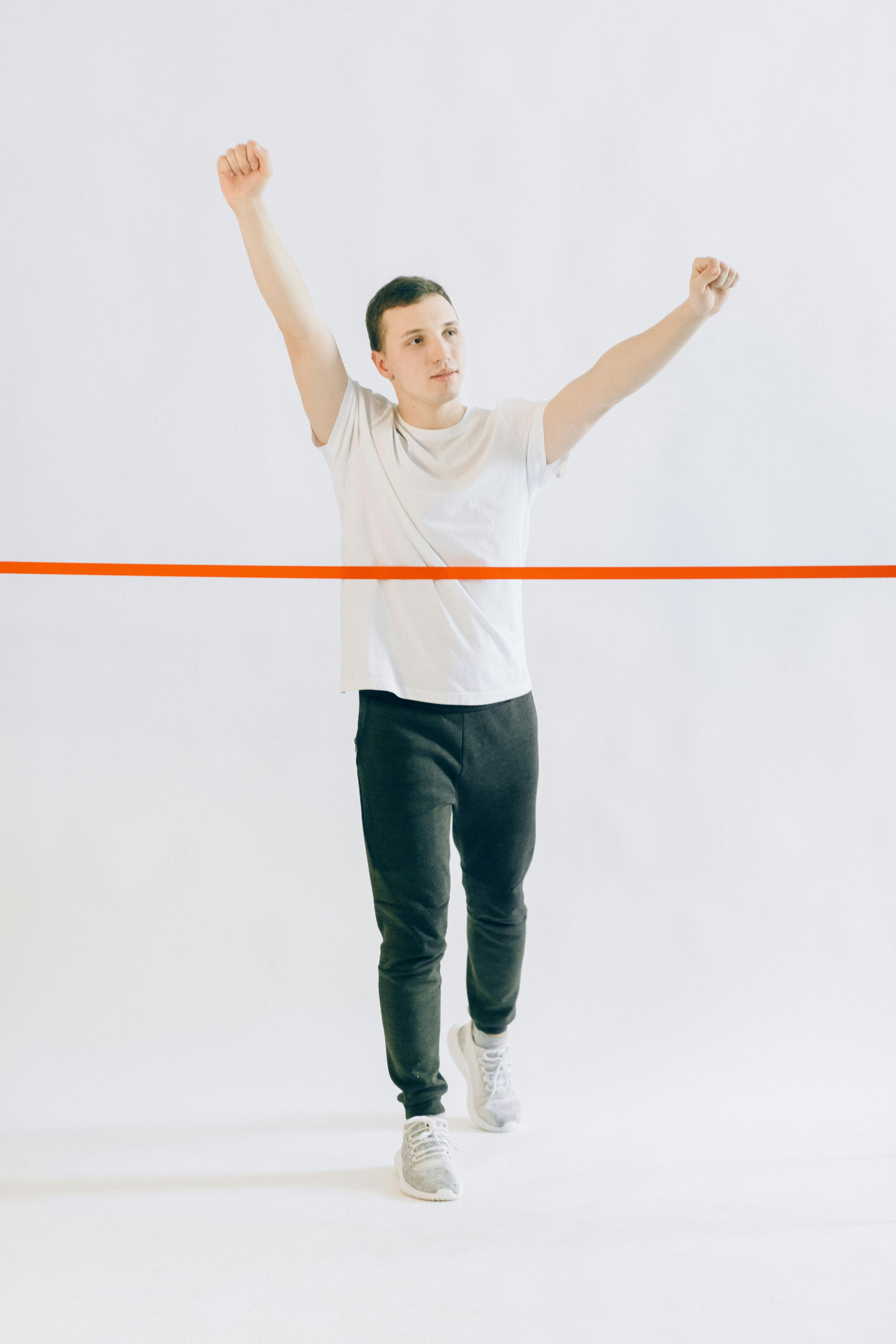 man in white crew neck shirt and black pants raising his arms