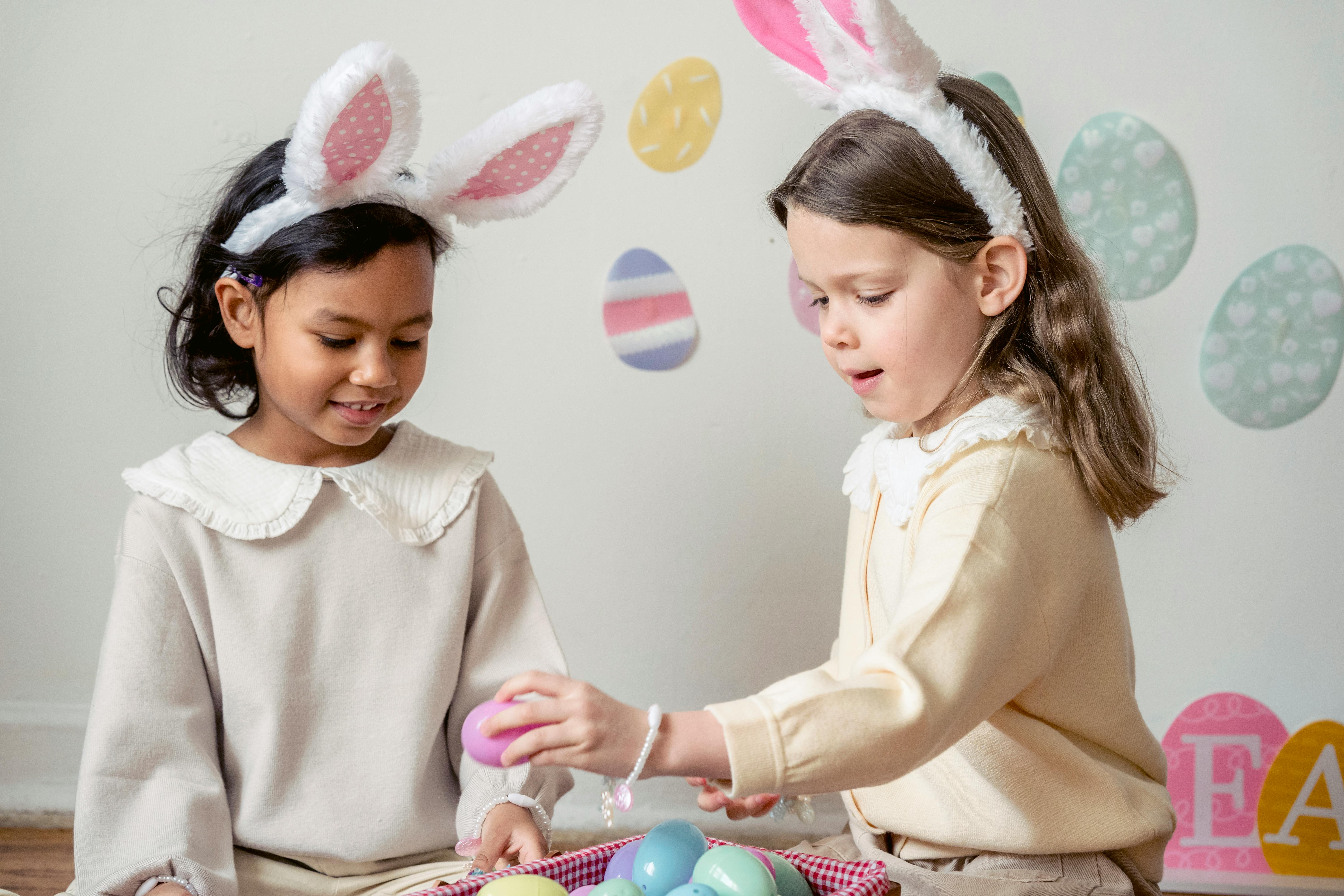 happy diverse girls in bunny ears playing with eggs