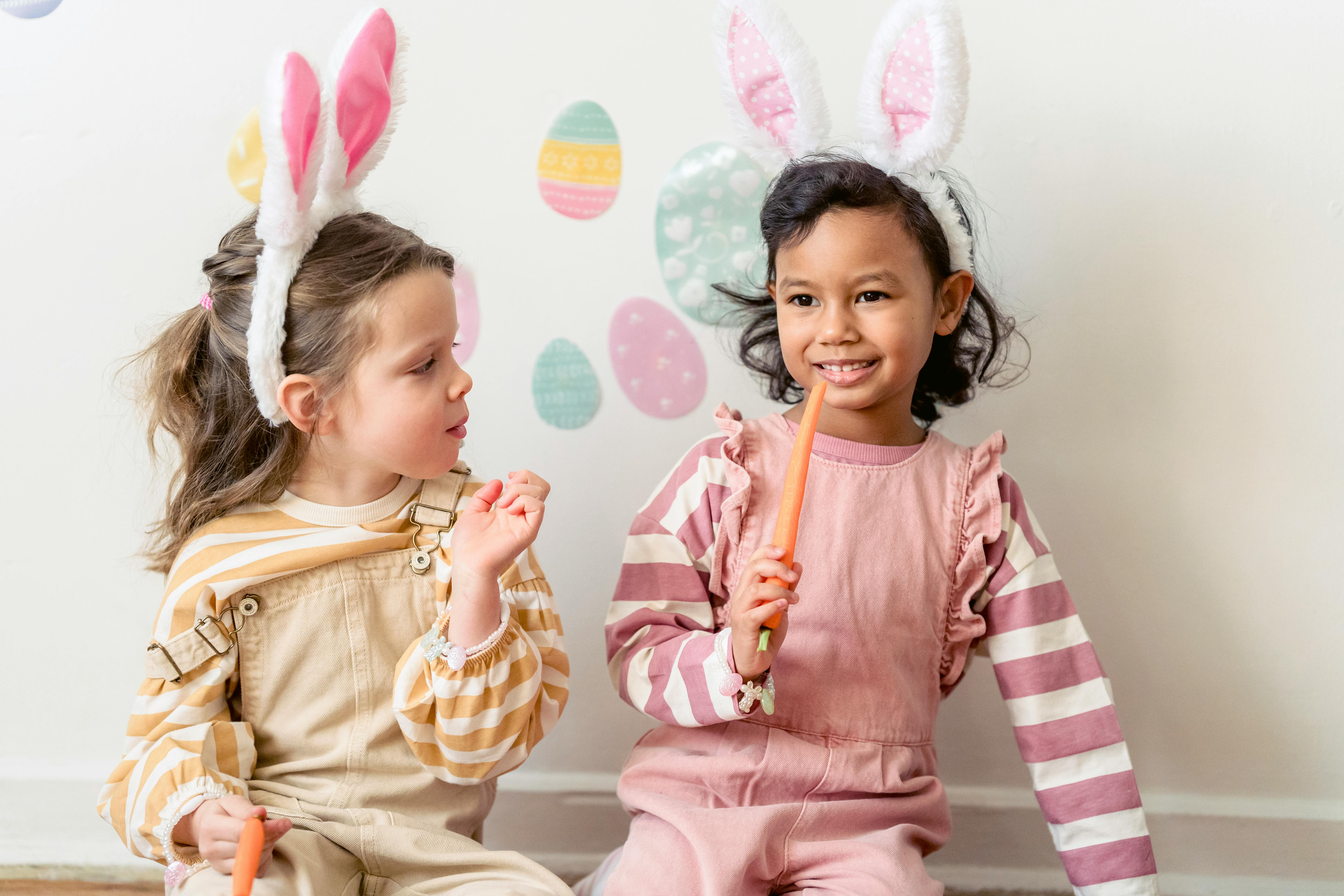 cheerful ethnic girl with carrot sitting near friend