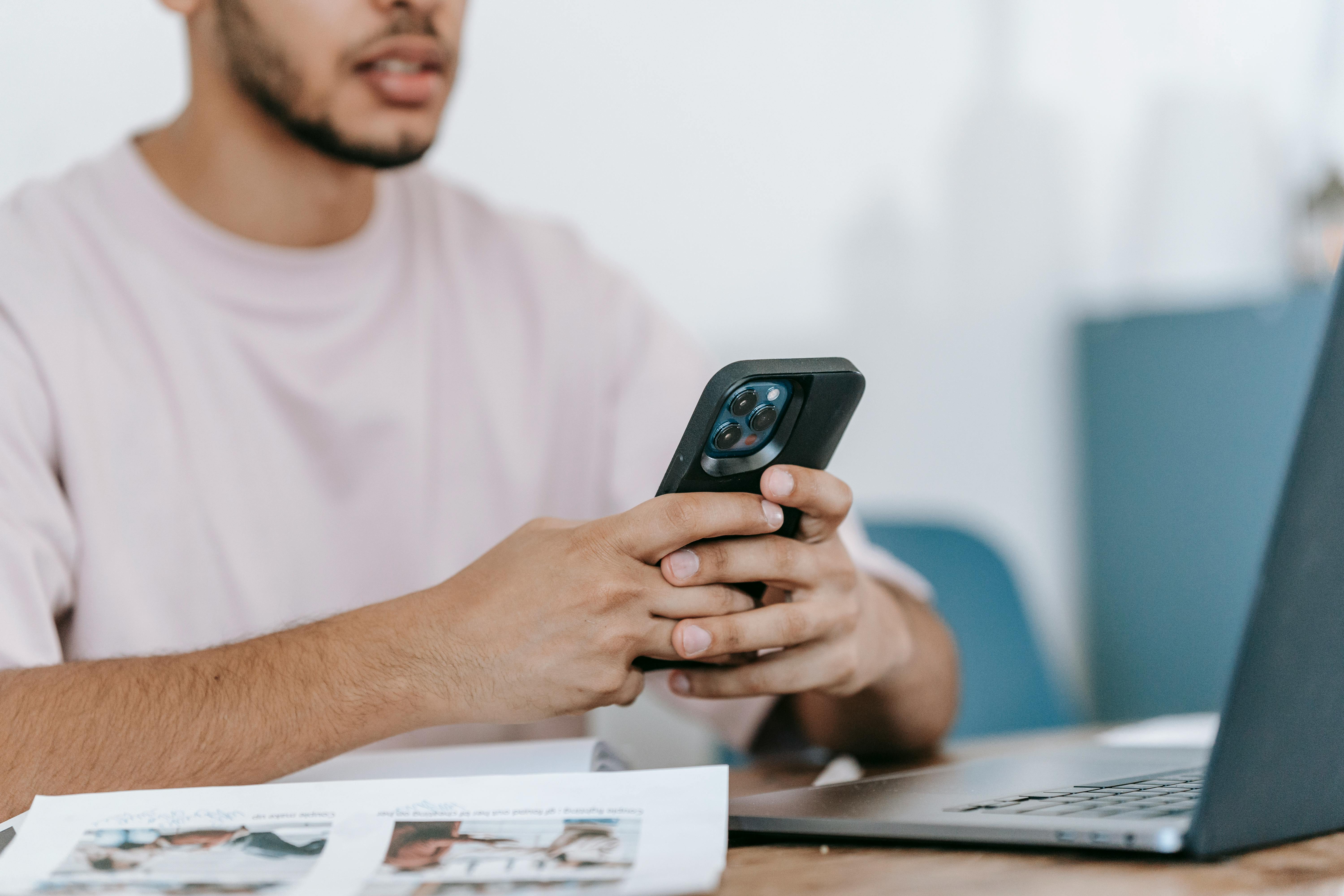 crop man using smartphone and laptop at desk