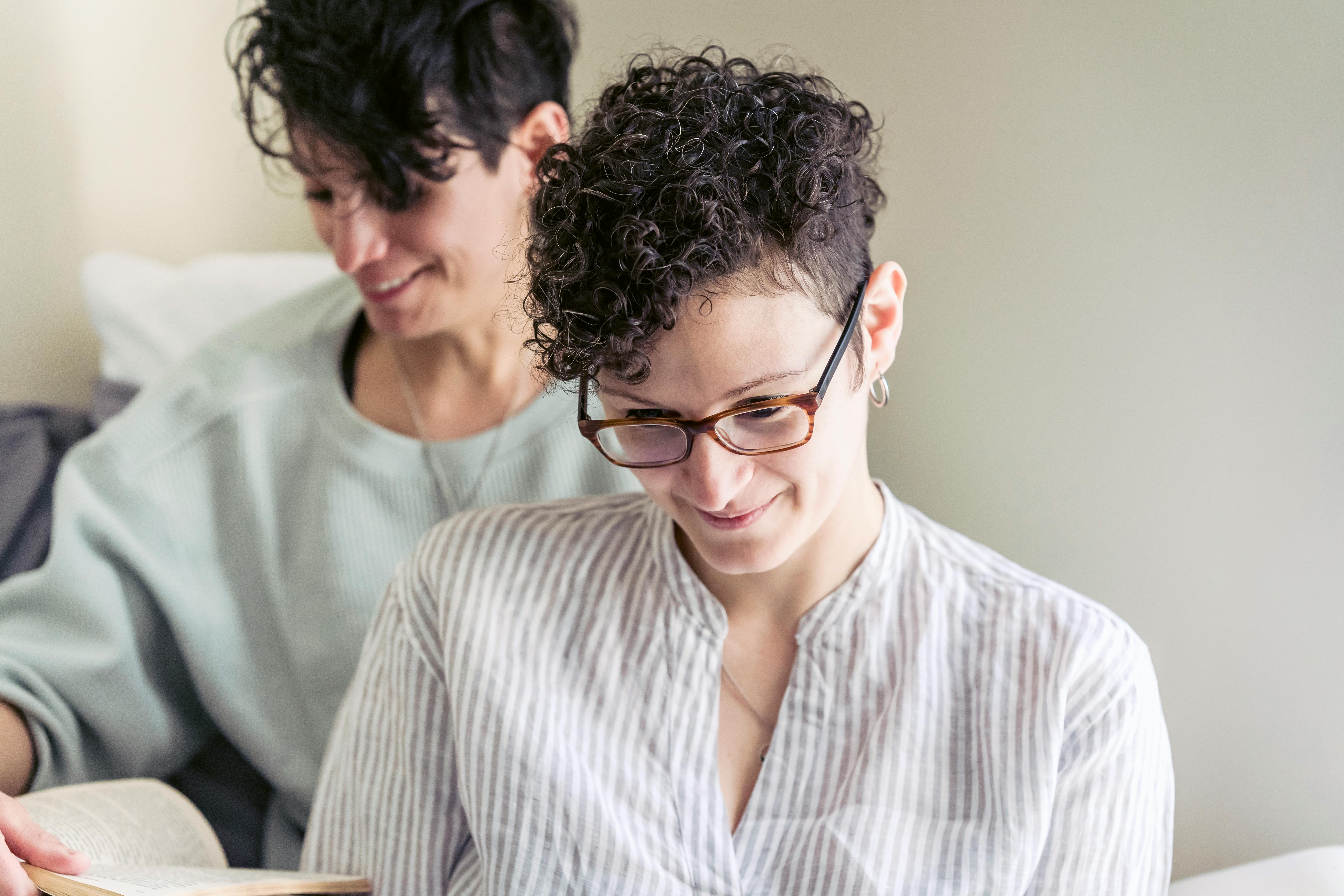 crop smiling girlfriends with book at home