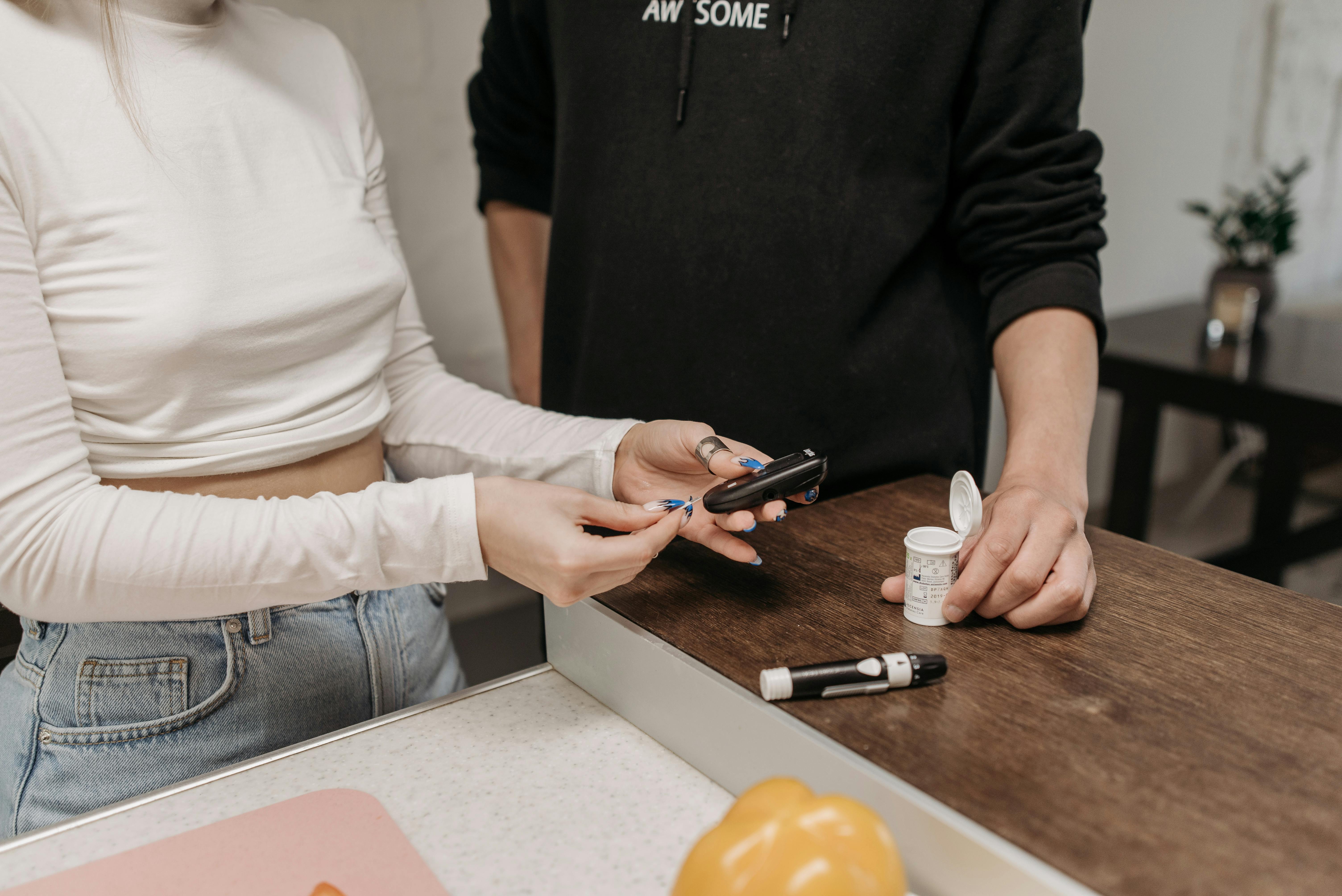 close up shot of a woman in beige long sleeves preparing the glucose meter while standing beside a person wearing black hoodieb