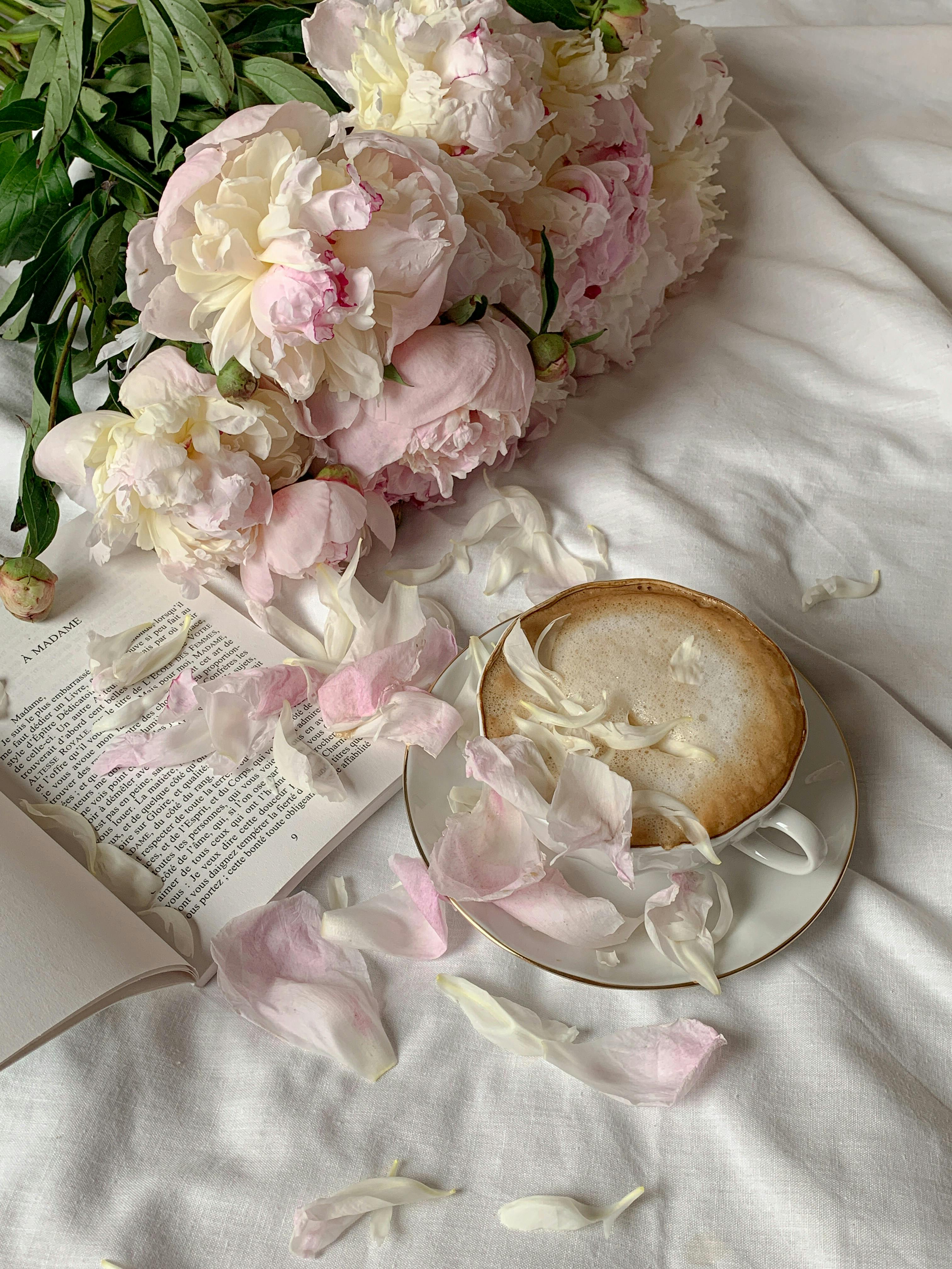 pink petals on the cup of coffee and book