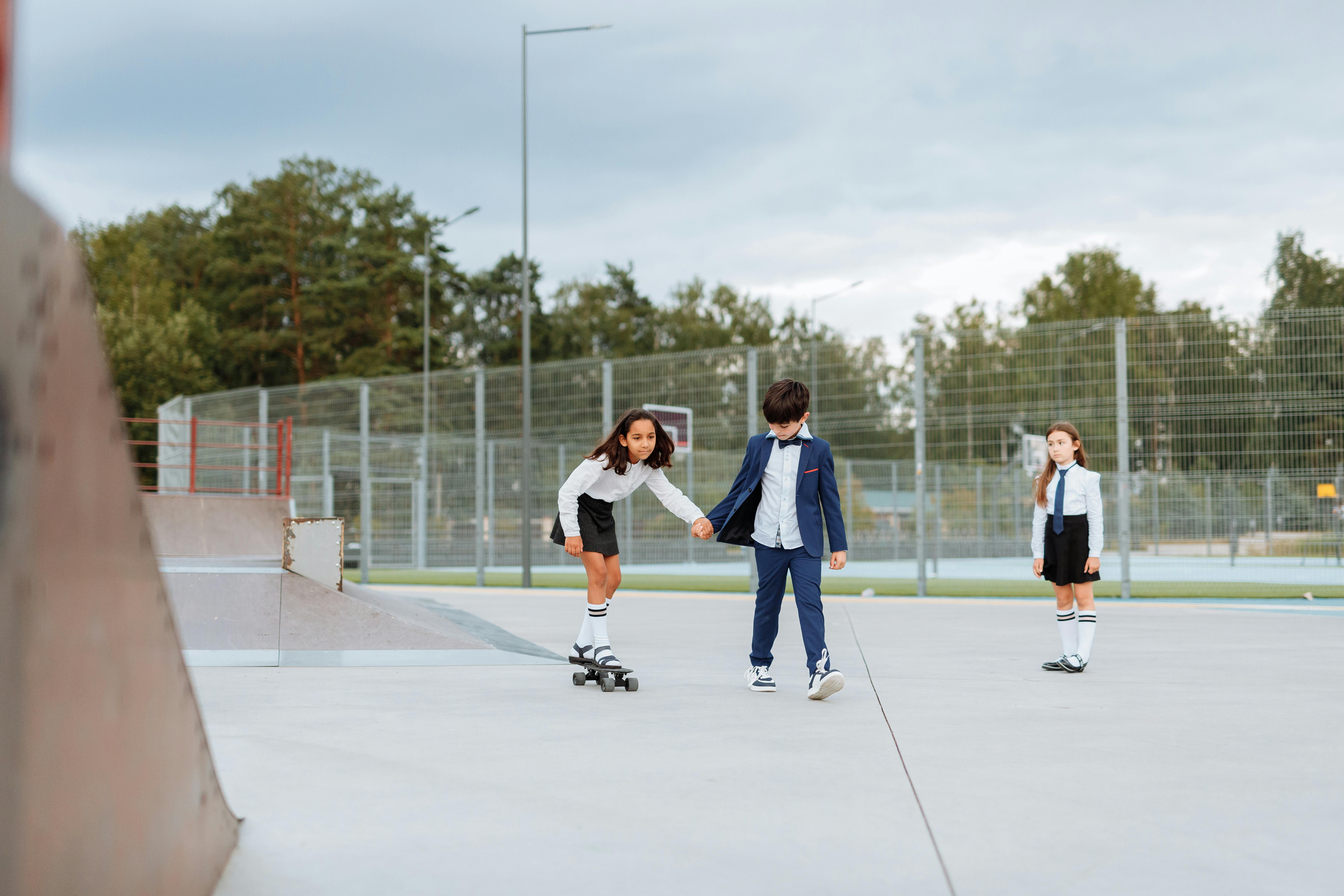 girl holding the hand of a boy while riding a penny board