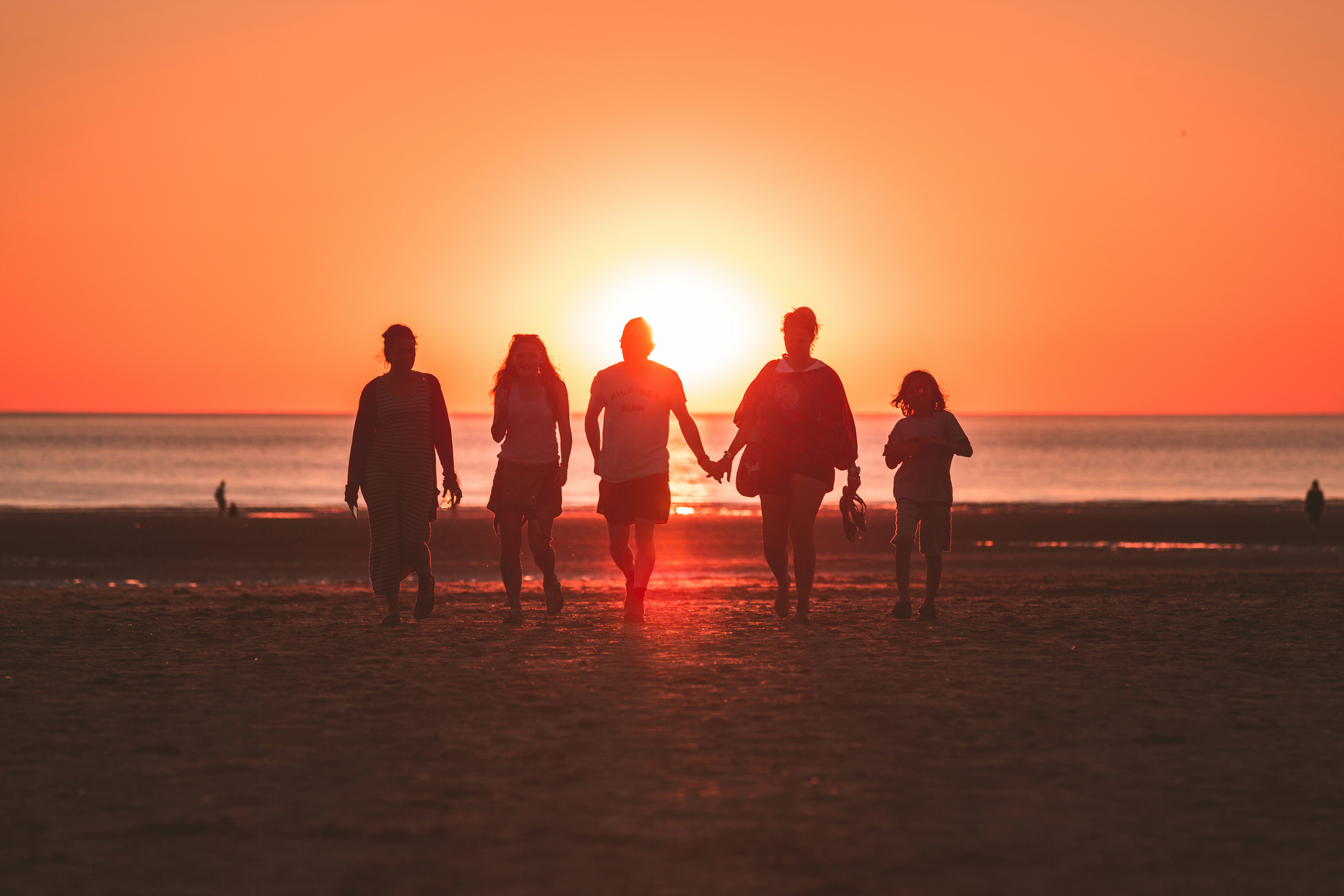 silhouette photo of five person walking on seashore during golden hour