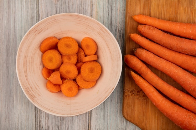 Free photo top view of highly nutritious carrots on a wooden kitchen board with chopped carrots on a bowl on a grey wooden wall