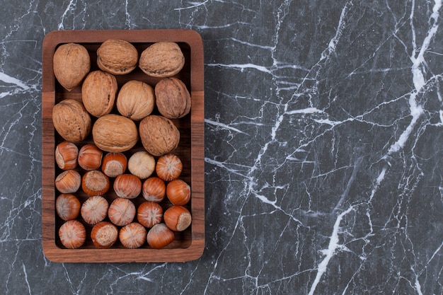 Free photo top view. pile of walnut and hazelnut on wooden plate over black.