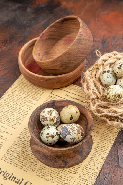 Free photo vertical view of fresh eggs from a basket with towel and old newspaper wooden pots on a brown background