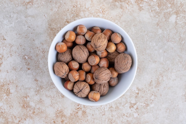 Free photo a white bowl full of healthy macadamia nuts and walnuts placed on a stone surface.