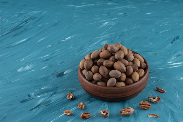 Free photo wooden bowl of shelled organic walnuts on blue surface.