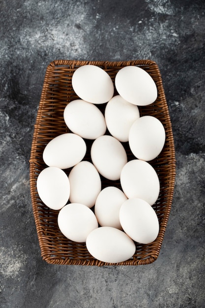 Free photo a wooden wicker full of white raw chicken eggs .