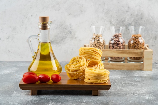 Free photo a bottle of oil with raw nest pasta and cherry tomatoes.