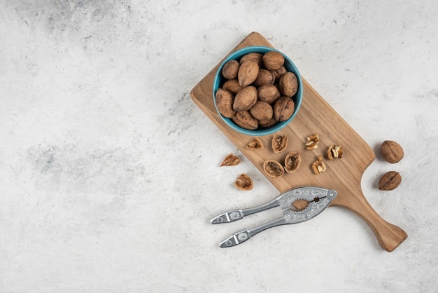 Free photo blue bowl of whole walnuts on wooden cutting board.