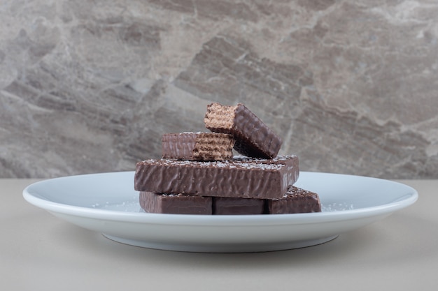 Free photo chocolate coated wafers stacked on a white platter on marble background.