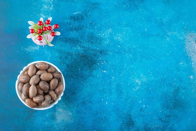 Free photo cherry fruits in a vase next to pecan nuts in a bowl , on the blue table.