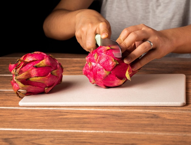 Free photo closeup of a person cutting a red dragon fruit in half on a cutting board on the table