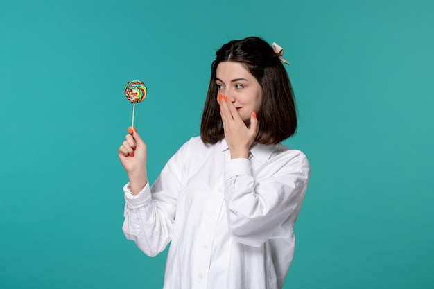 Free photo cute girl pretty brunette young sweet girl in white shirt covering mouth with lollipop