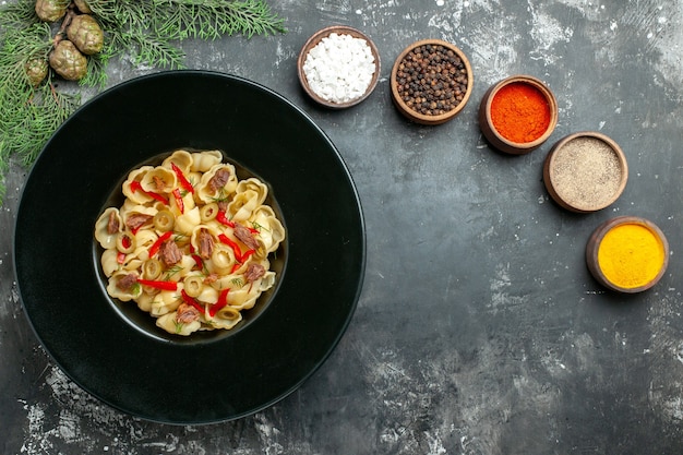 Free photo overhead view of delicious conchiglie with vegetables and greens on a plate and knife and different spices on gray background