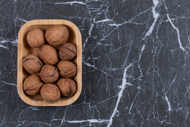 Free photo pile of walnut in wooden bowl over black.