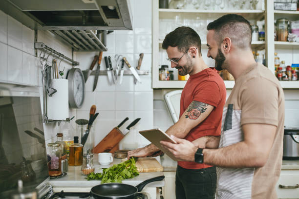 mann steht bei einem freund, der zu hause essen zubereitet - boy friend stock-fotos und bilder