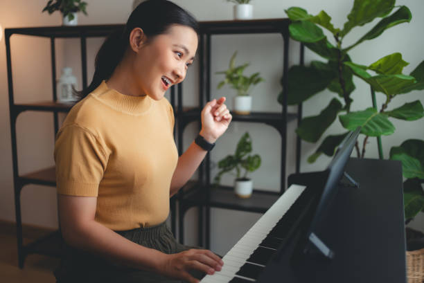 asian woman learning to play the piano watching video clips from tablet. - video clips stockfoto's en -beelden