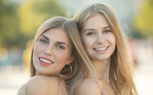 Two attractive young girl friends standing together and posing on camera. - Stock Image